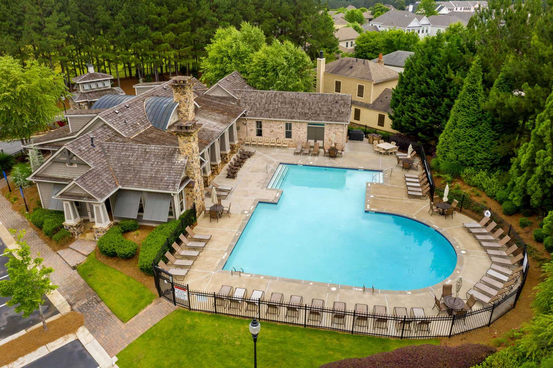 Resort-style swimming pool and stone clubhouse at The Village at Towne Lake in Woodstock GA with lounge seating and lush greenery