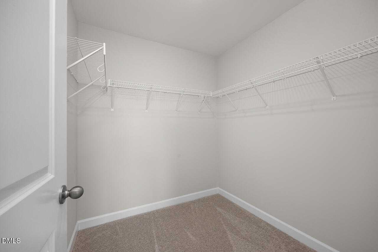 Spacious walk-in closet with wire shelving and carpeted floor in Davidson Homes The Warren plan, Fuquay-Varina, NC