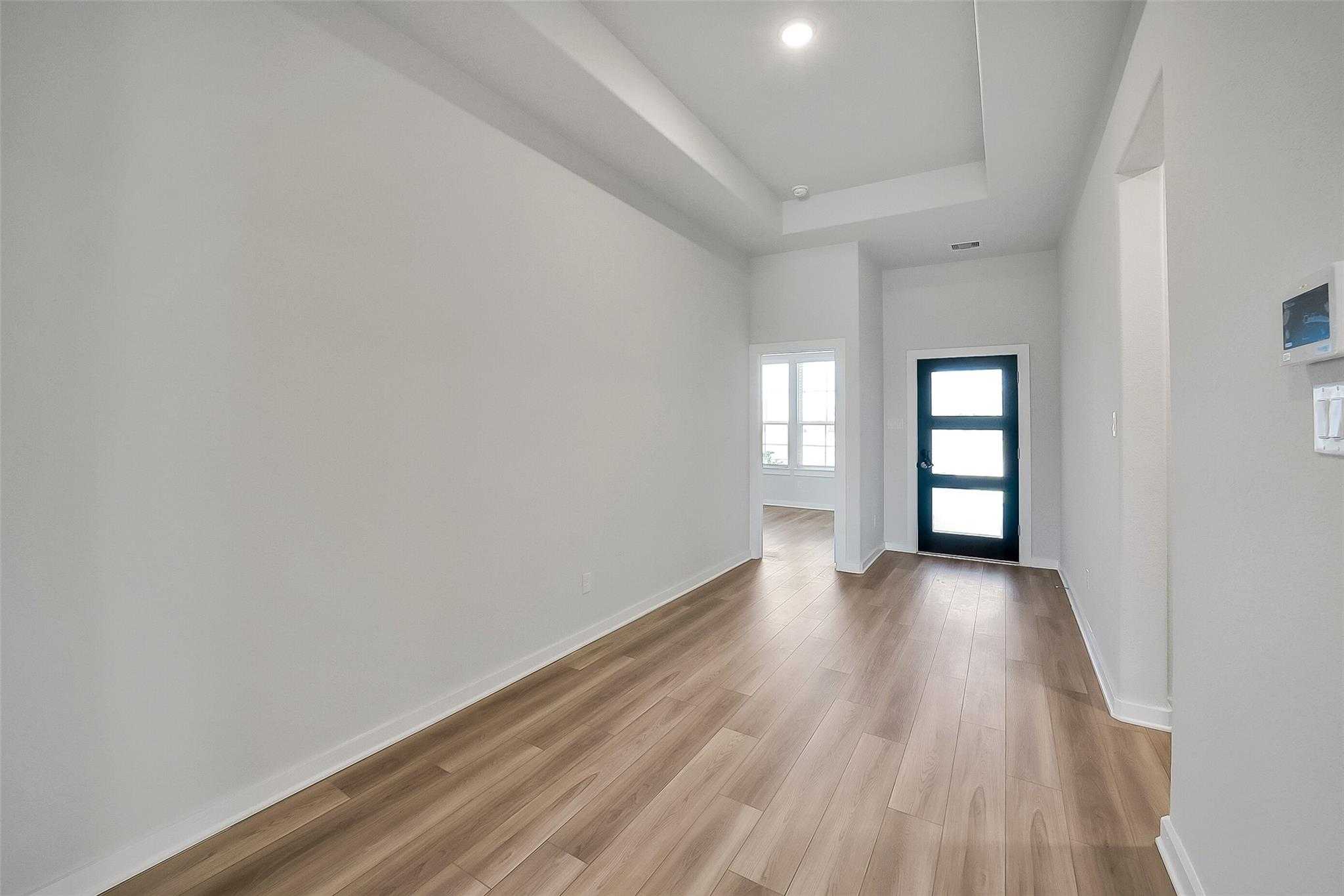 Spacious hallway with tray ceiling, light wood floors, and navy glass door in Davidson Homes Acadia A, Sunterra, Katy, Texas