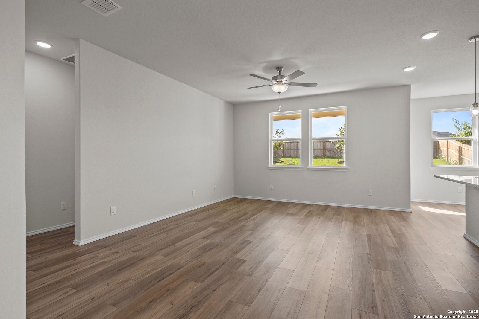 Open living room with wood flooring, ceiling fan, large windows overlooking backyard in Davidson Homes The Asheville J, San Antonio