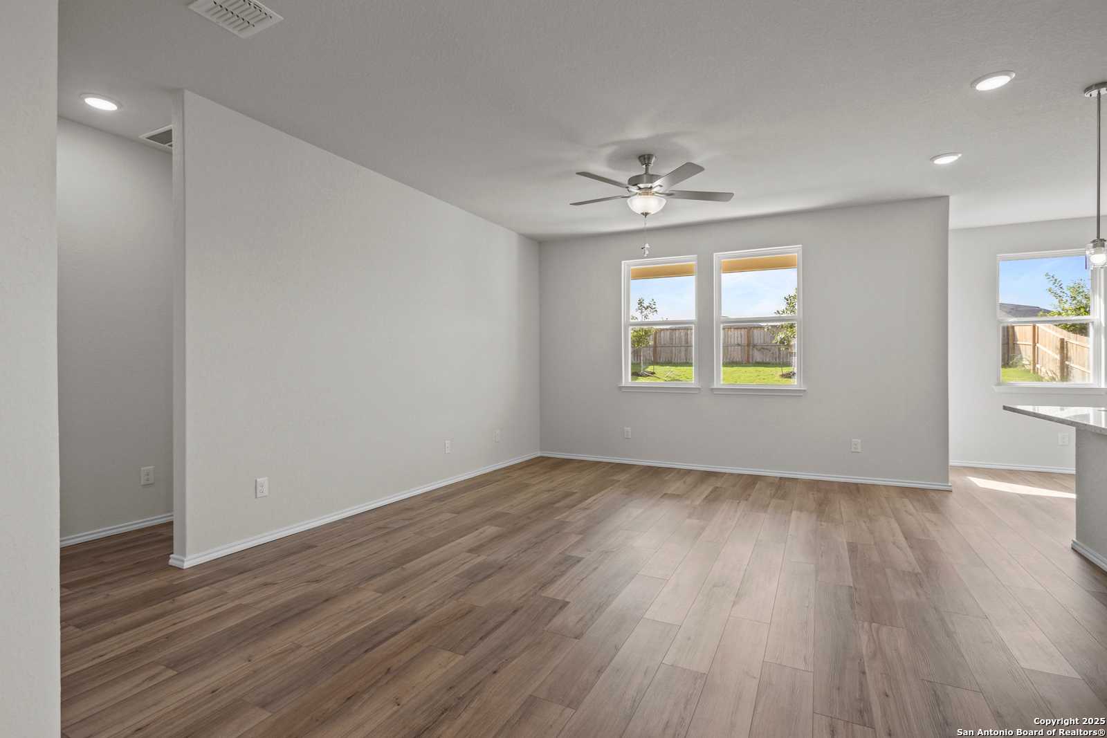 Open living room with wood flooring, ceiling fan, large windows overlooking backyard in Davidson Homes The Asheville J, San Antonio