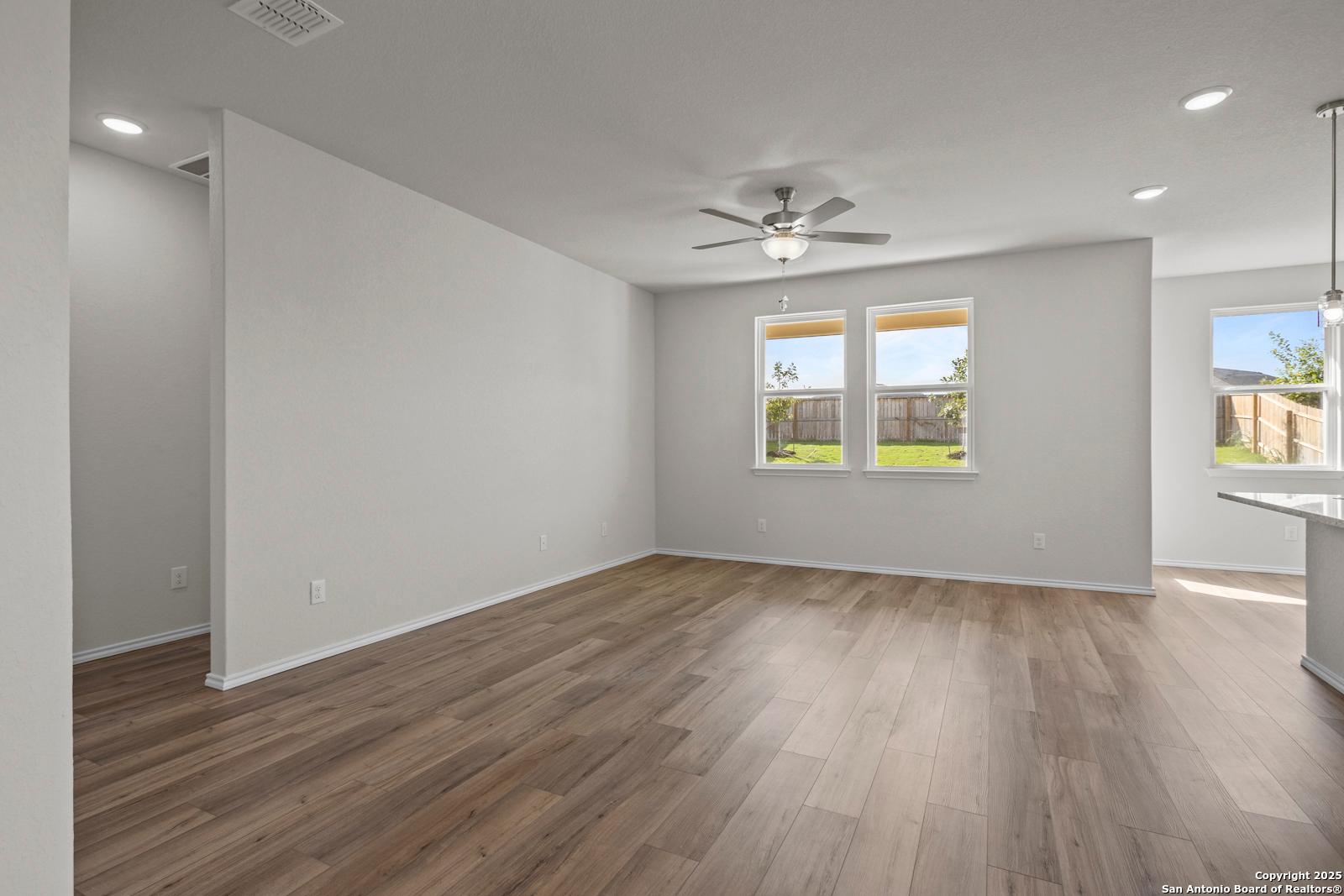 Open living room with wood flooring, ceiling fan, large windows overlooking backyard in Davidson Homes The Asheville J, San Antonio