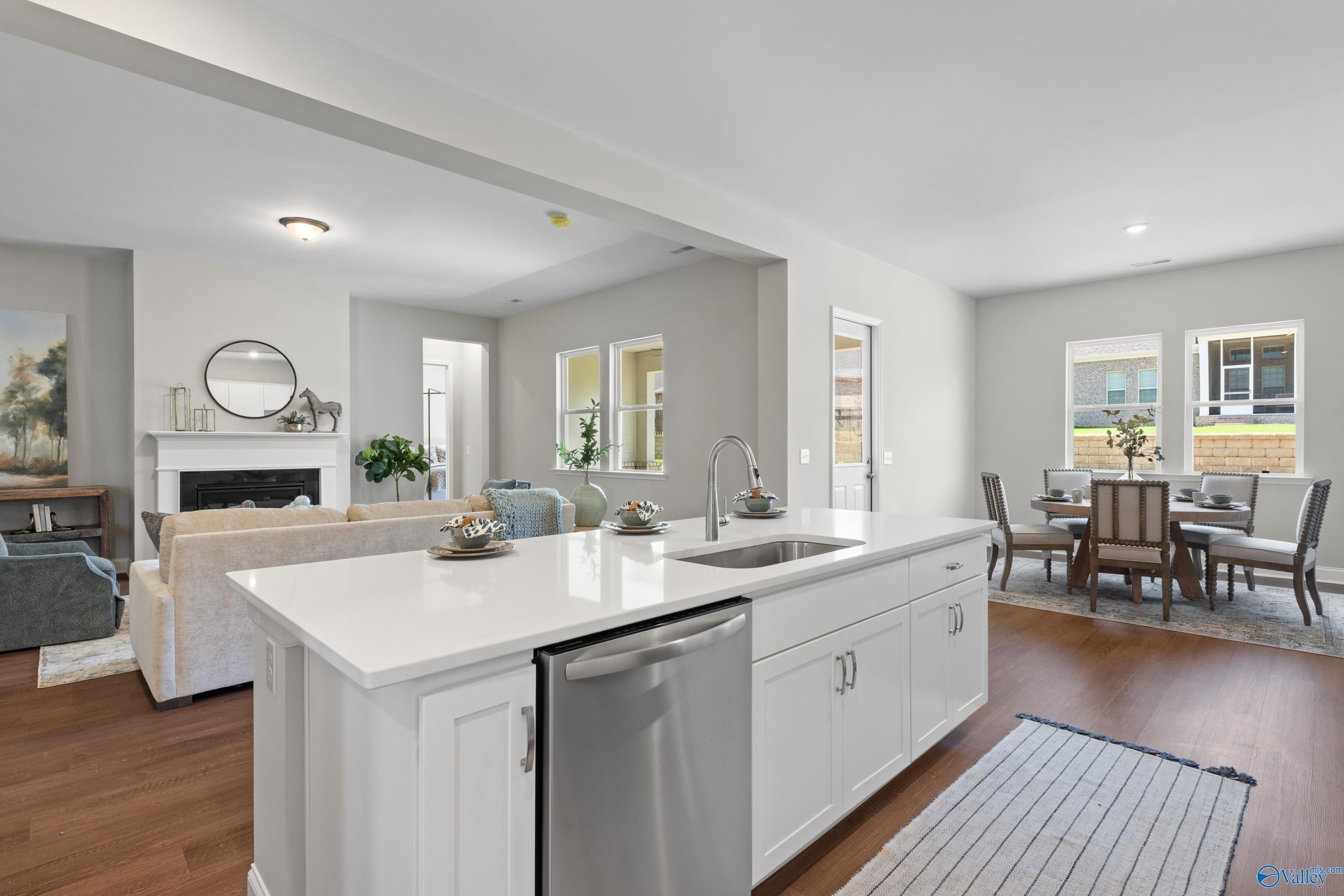 Modern open-concept kitchen with white island, stainless dishwasher, and dining area beside cozy living room fireplace in Evermore Homes The Haven, Owens Cross Roads