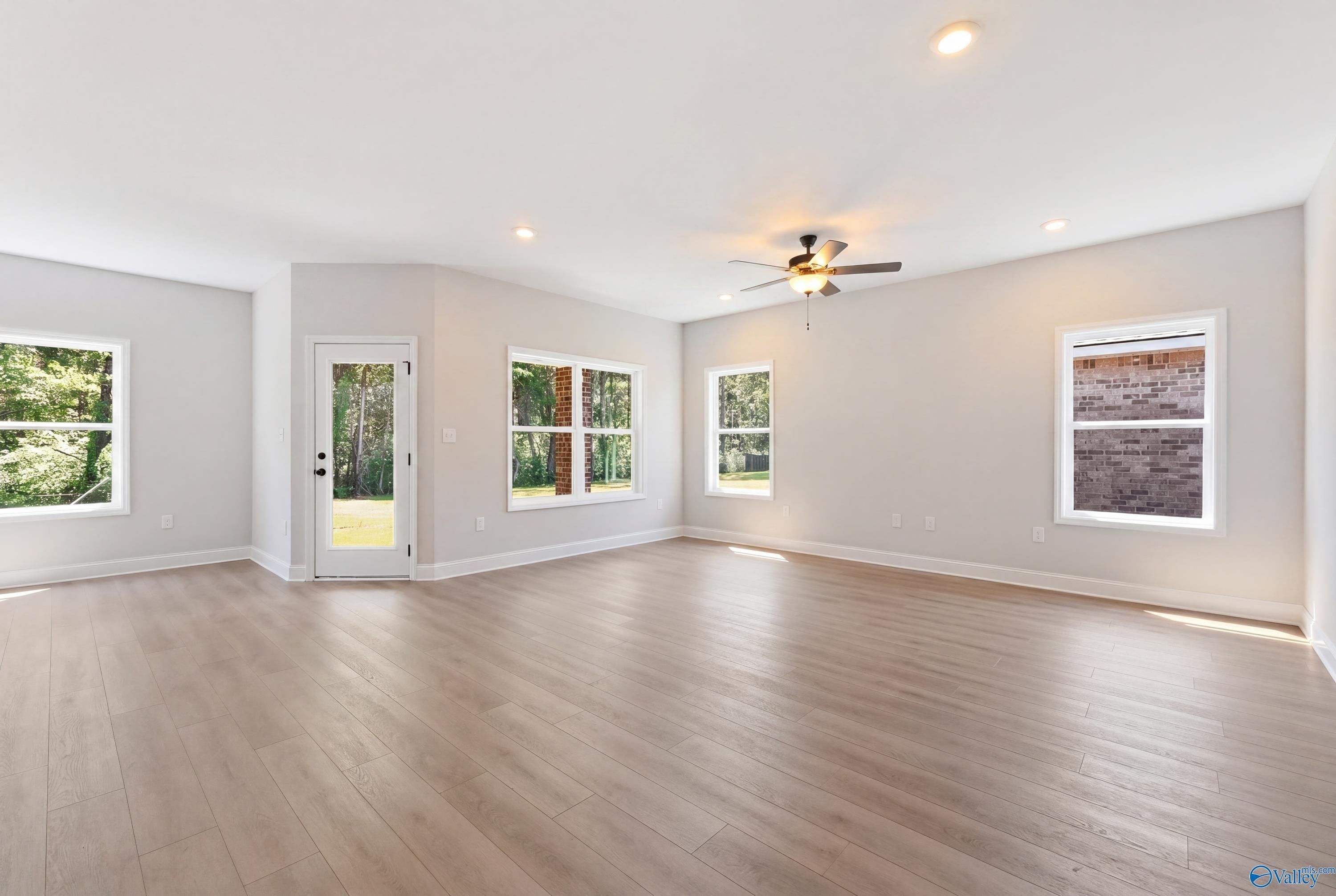 Spacious living room with large windows, glass door to backyard, ceiling fans, light wood floors in The Franklin home, Huntsville AL