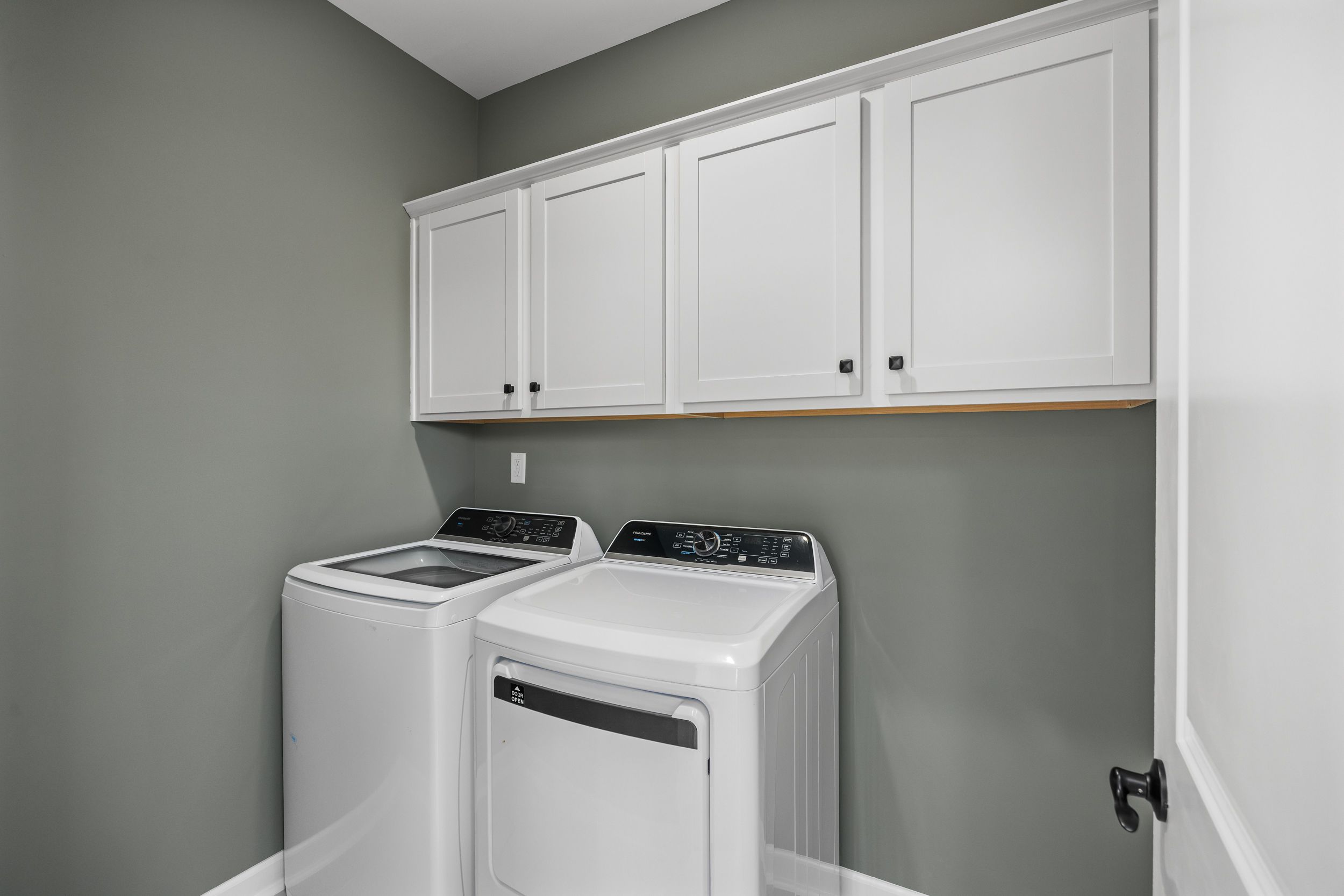 Spacious laundry room at Forestville Yard in Knightdale NC featuring white washer dryer and shaker cabinets on gray walls