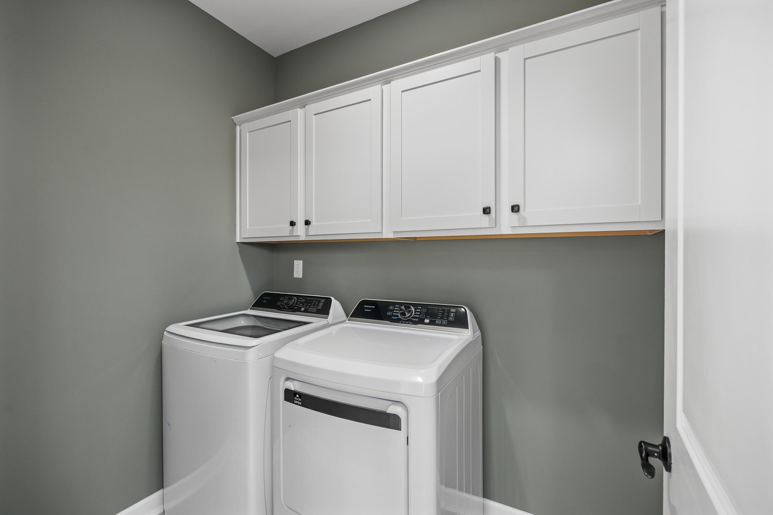 Spacious laundry room at Forestville Yard in Knightdale NC featuring white washer dryer and shaker cabinets on gray walls