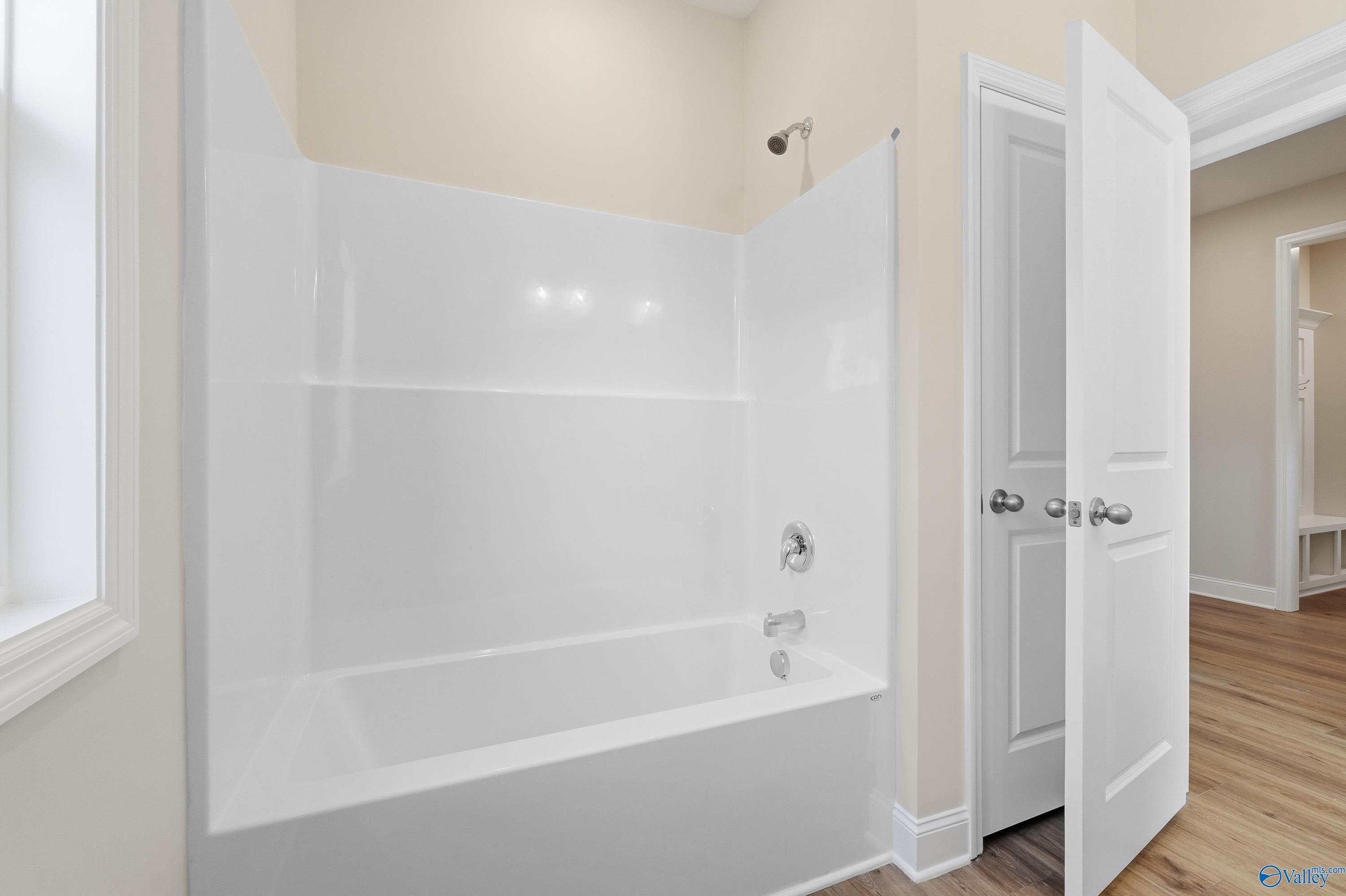 Modern bathroom with white tiled walk-in shower, deep soaking tub, and hardwood floors in Davidson Homes The Everett, Harvest, Alabama