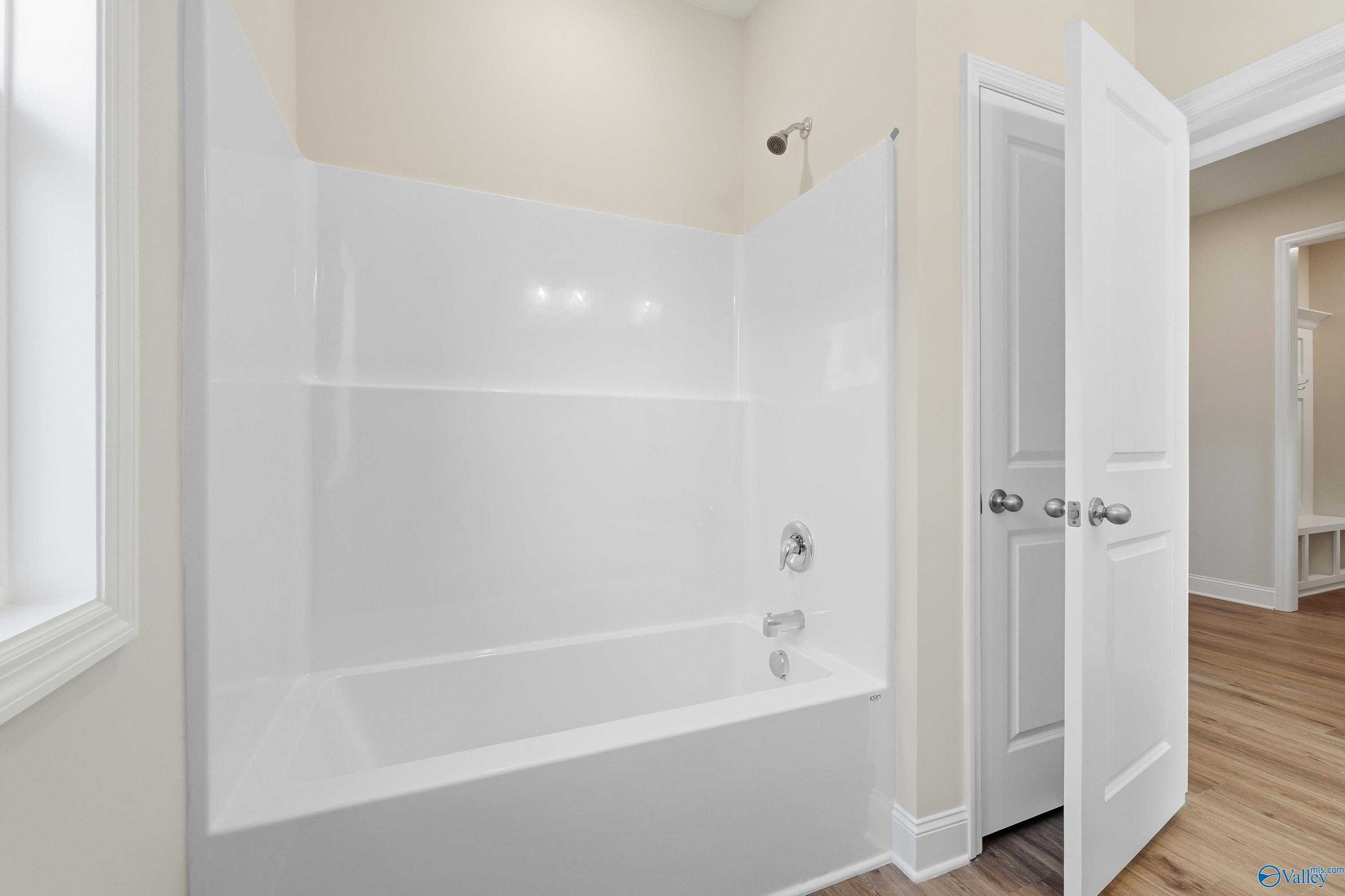 Modern bathroom with white tiled walk-in shower, deep soaking tub, and hardwood floors in Davidson Homes The Everett, Harvest, Alabama