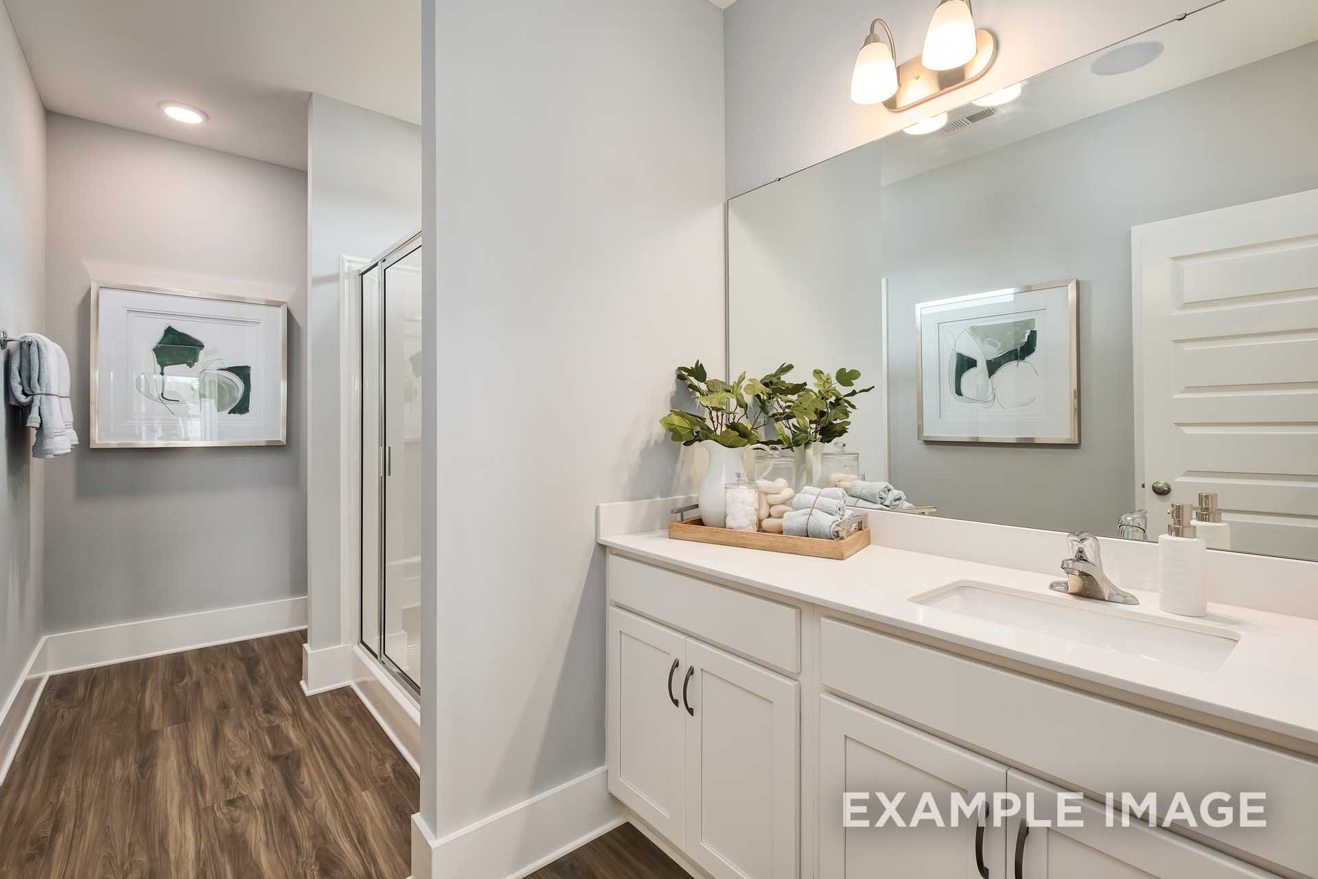 Spacious master bathroom in The Daphne D with white double vanity, frameless mirror, and walk-in glass shower