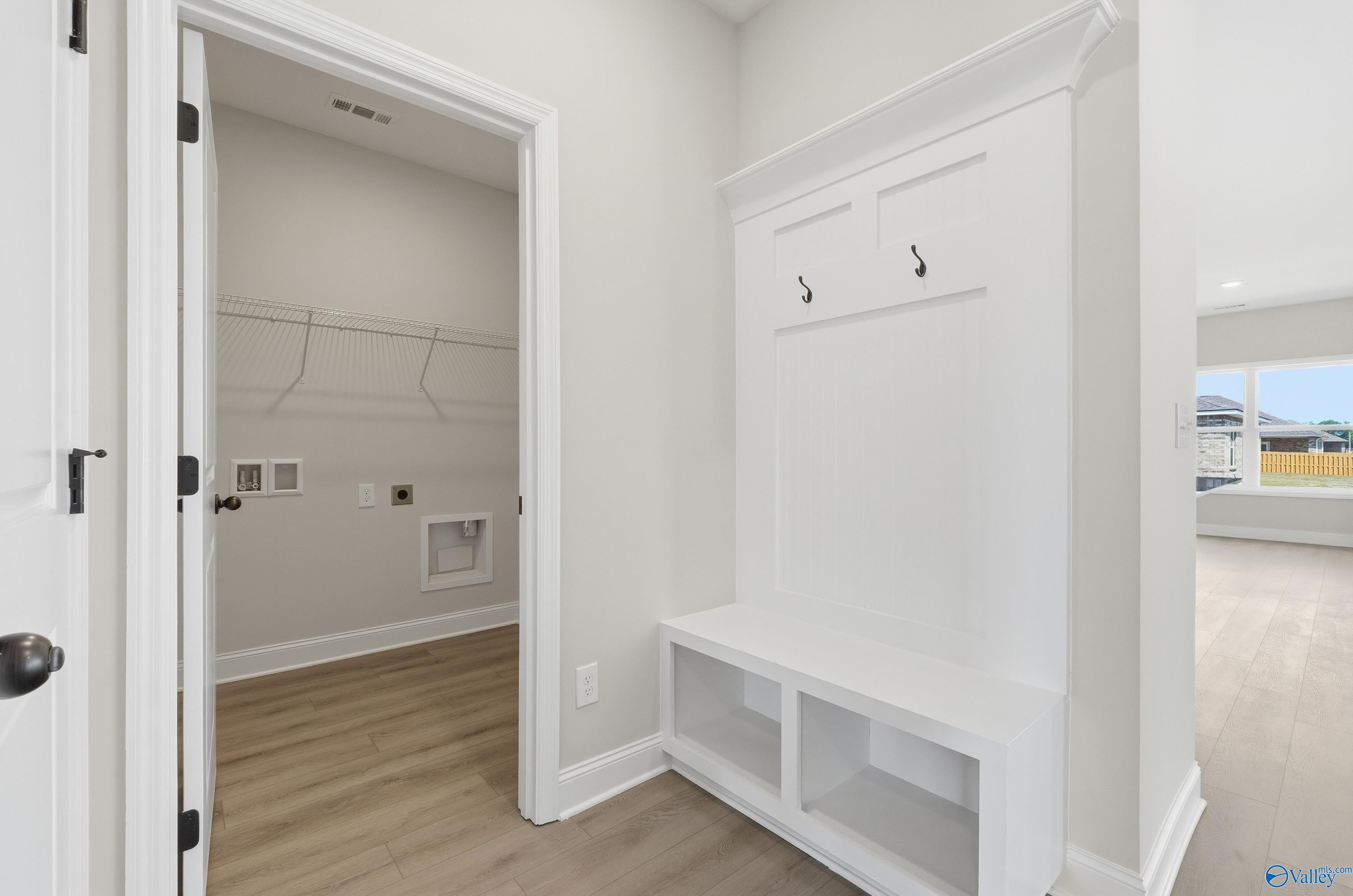 Functional mudroom with white built-in bench, coat hooks, wire shelving closet, and laundry sink in Davidson Homes The Franklin C, Meridianville, Alabama