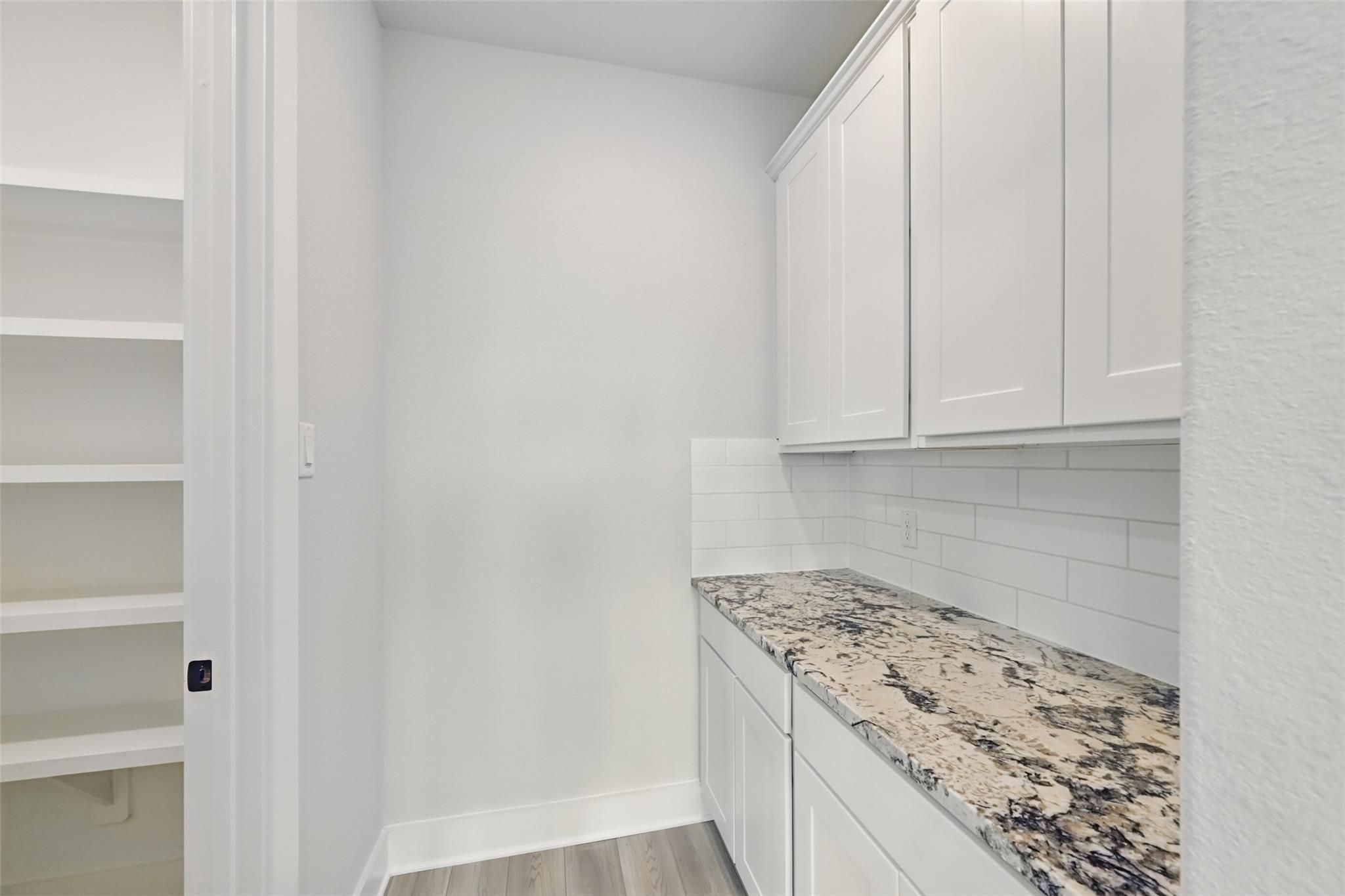 Modern laundry room featuring white cabinets, granite countertop, subway tile backsplash in Davidson Homes The Victoria C, Texas City