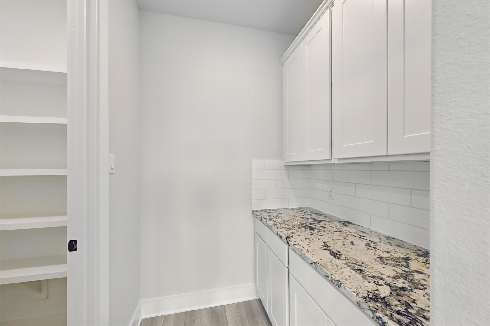 Modern laundry room featuring white cabinets, granite countertop, subway tile backsplash in Davidson Homes The Victoria C, Texas City