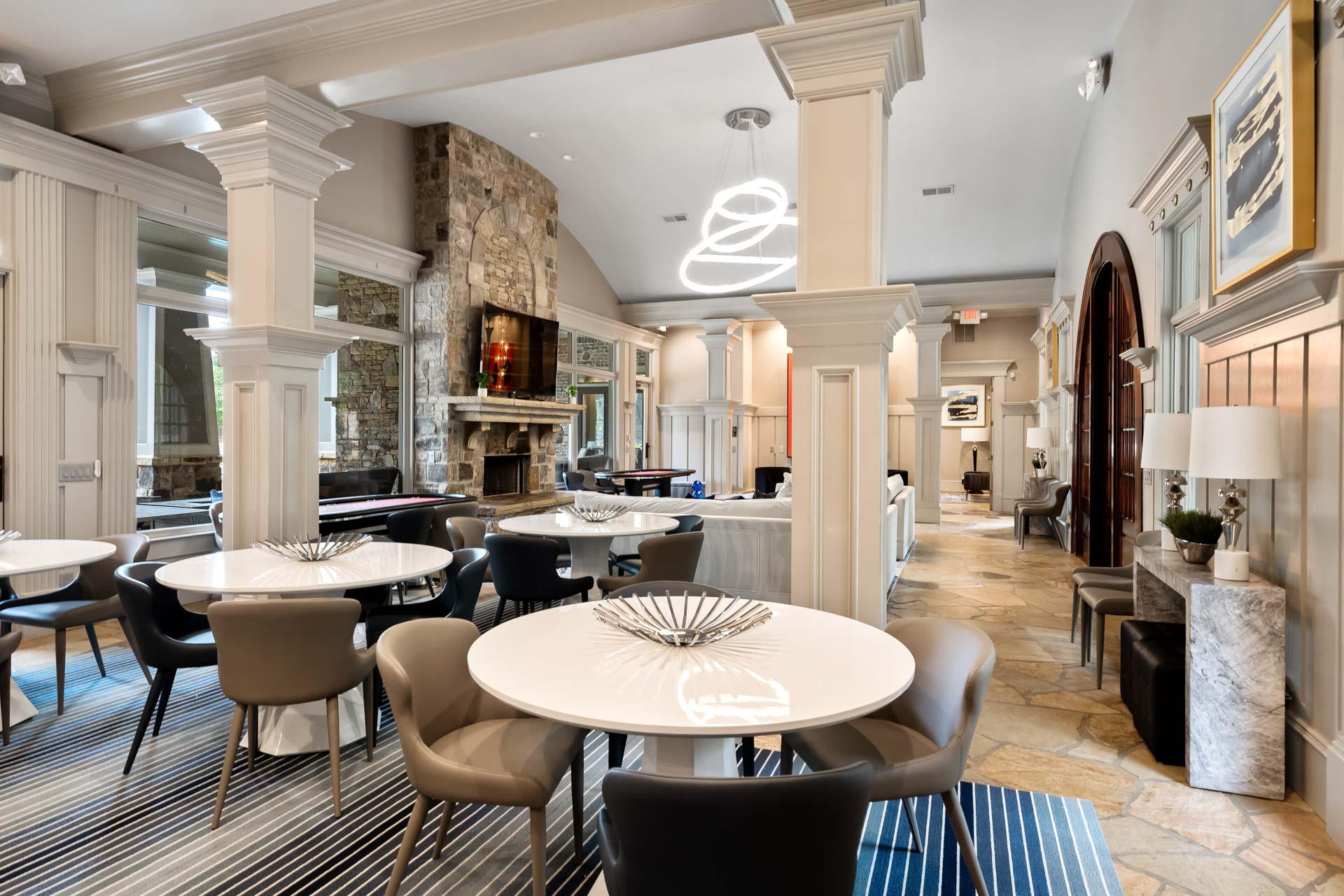 Elegant clubhouse lounge with stone fireplace, white columns, round tables, modern chairs and neon lighting at The Village at Towne Lake Woodstock GA