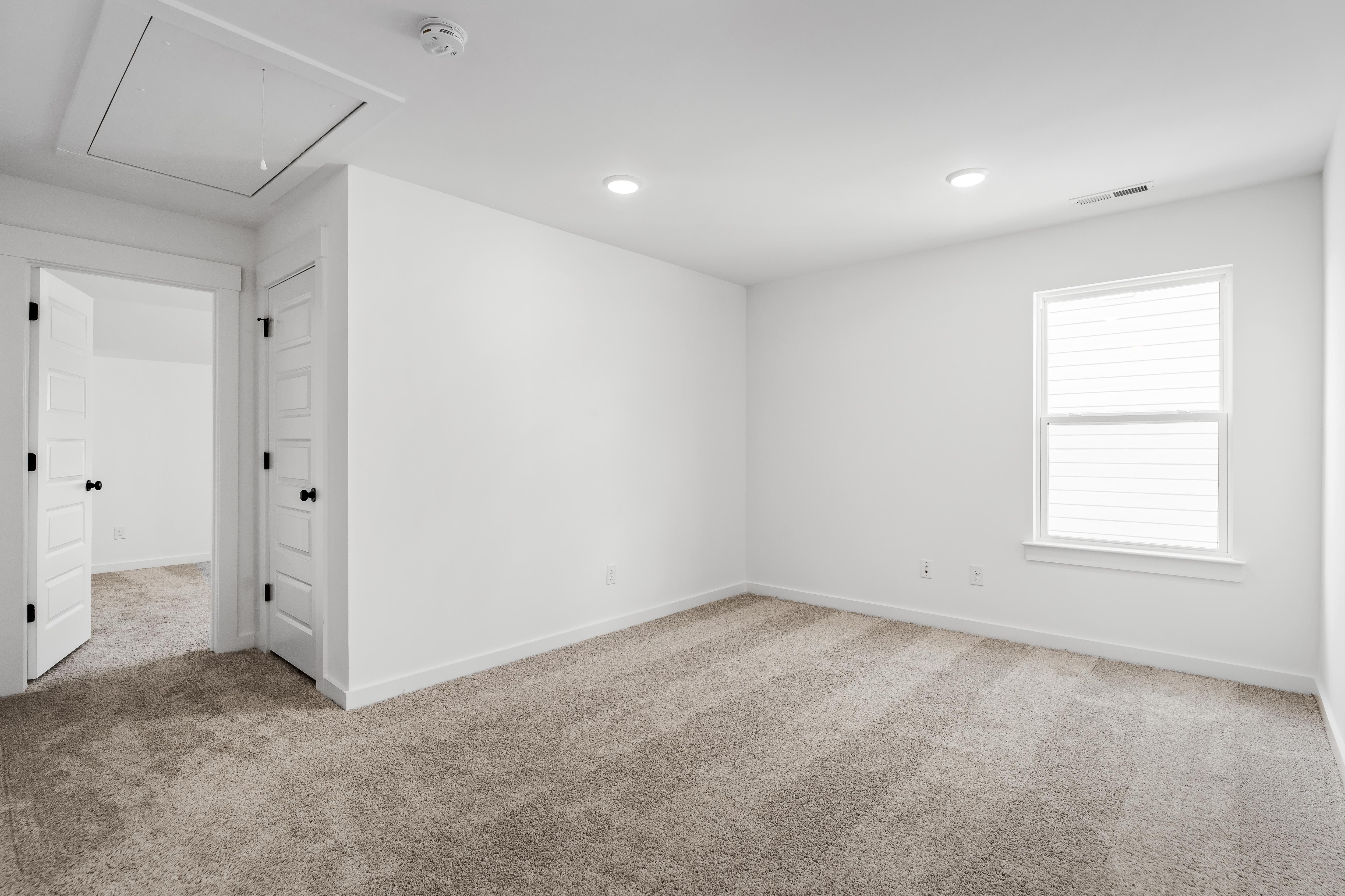 Bright, carpeted bedroom in The Cedar floor plan by Davidson Homes featuring clean white walls and recessed lighting.