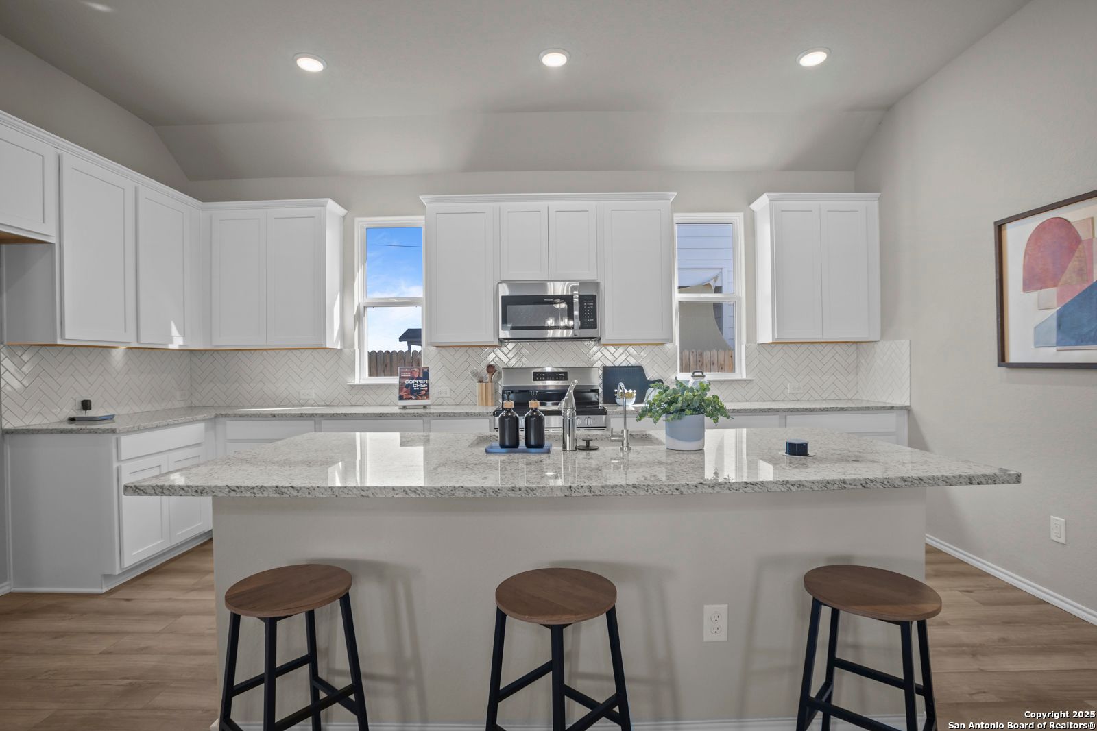 Modern white kitchen with granite countertops, stainless appliances, and island bar stools in The Collin B, Seguin TX