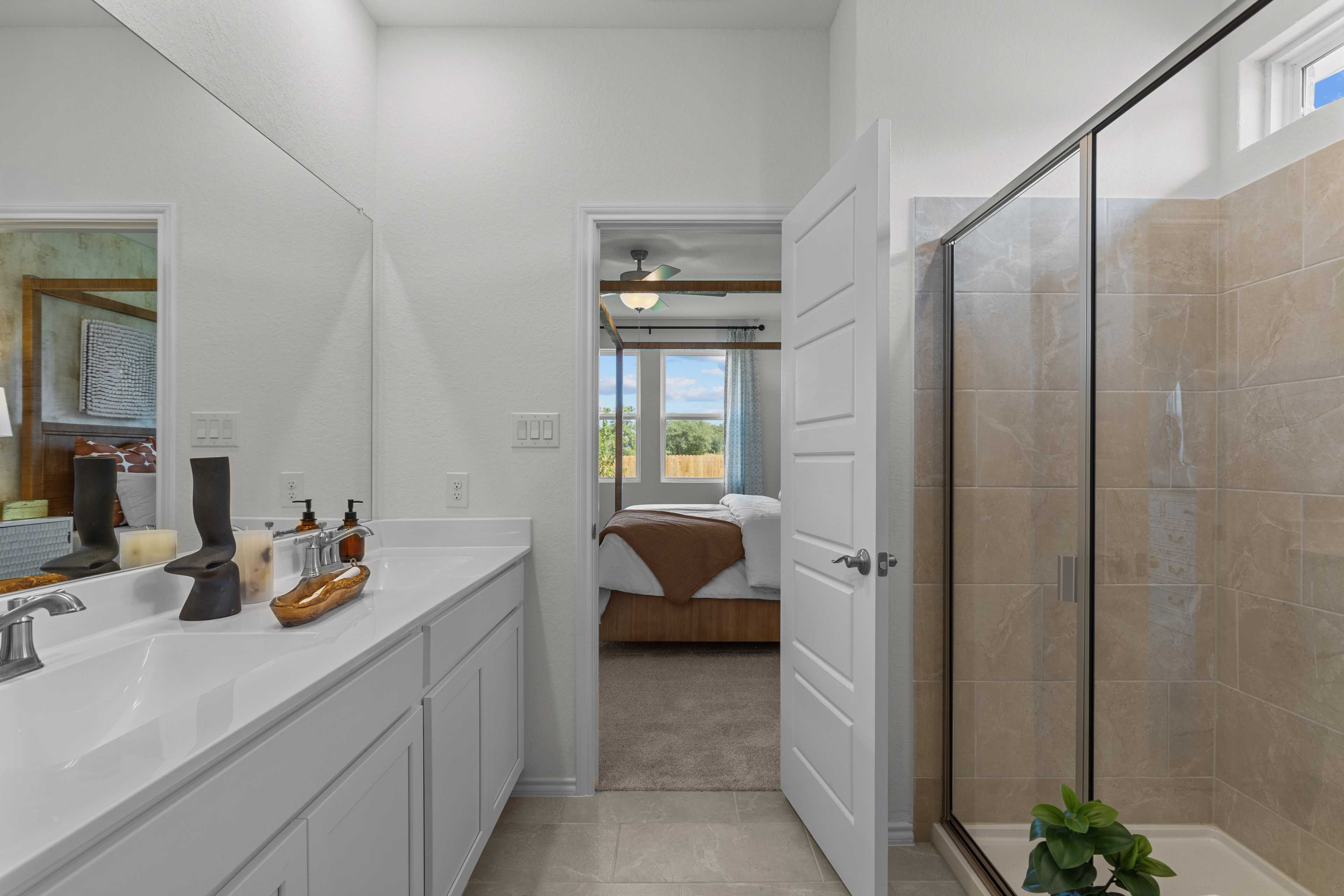 Spacious master bathroom in The Daphne H featuring double white vanity, large mirror, and beige-tiled walk-in shower
