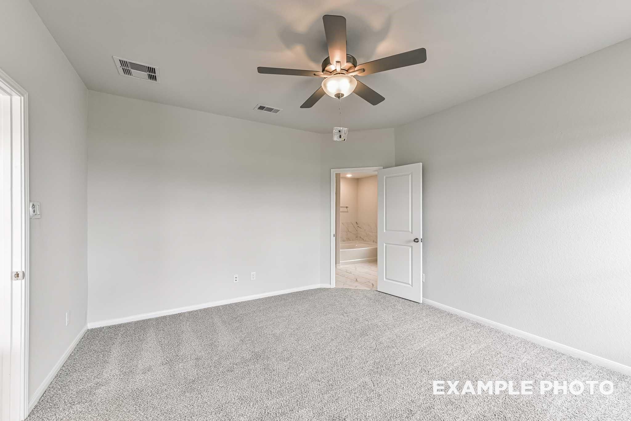 Spacious primary bedroom with ceiling fan and attached bathroom in The Costa A floor plan at Emberly, Beasley, Texas.