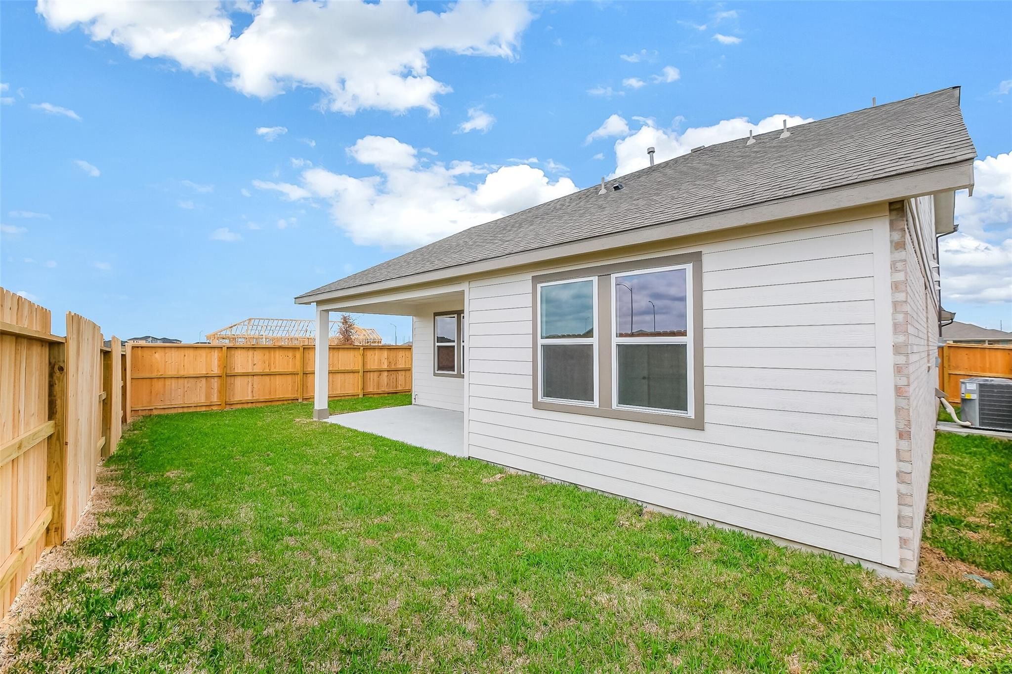 Modern two-story Tierra B home side exterior with covered patio, double windows, green lawn, and wood privacy fence in Beasley, Texas