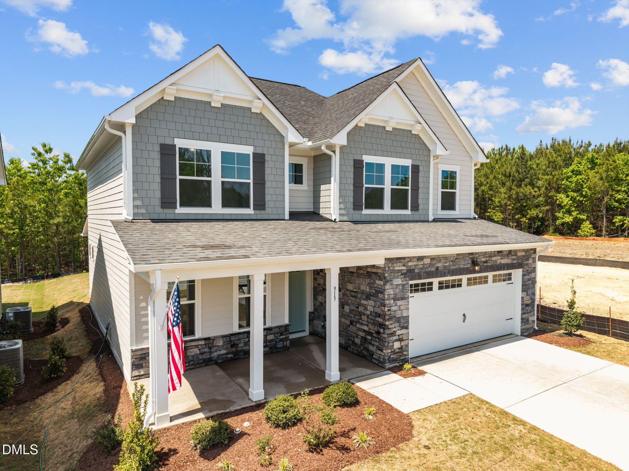 Modern two-story gray home with stone accents, covered porch, American flag, 2-car garage in Wendell Ridge, NC by Davidson Homes