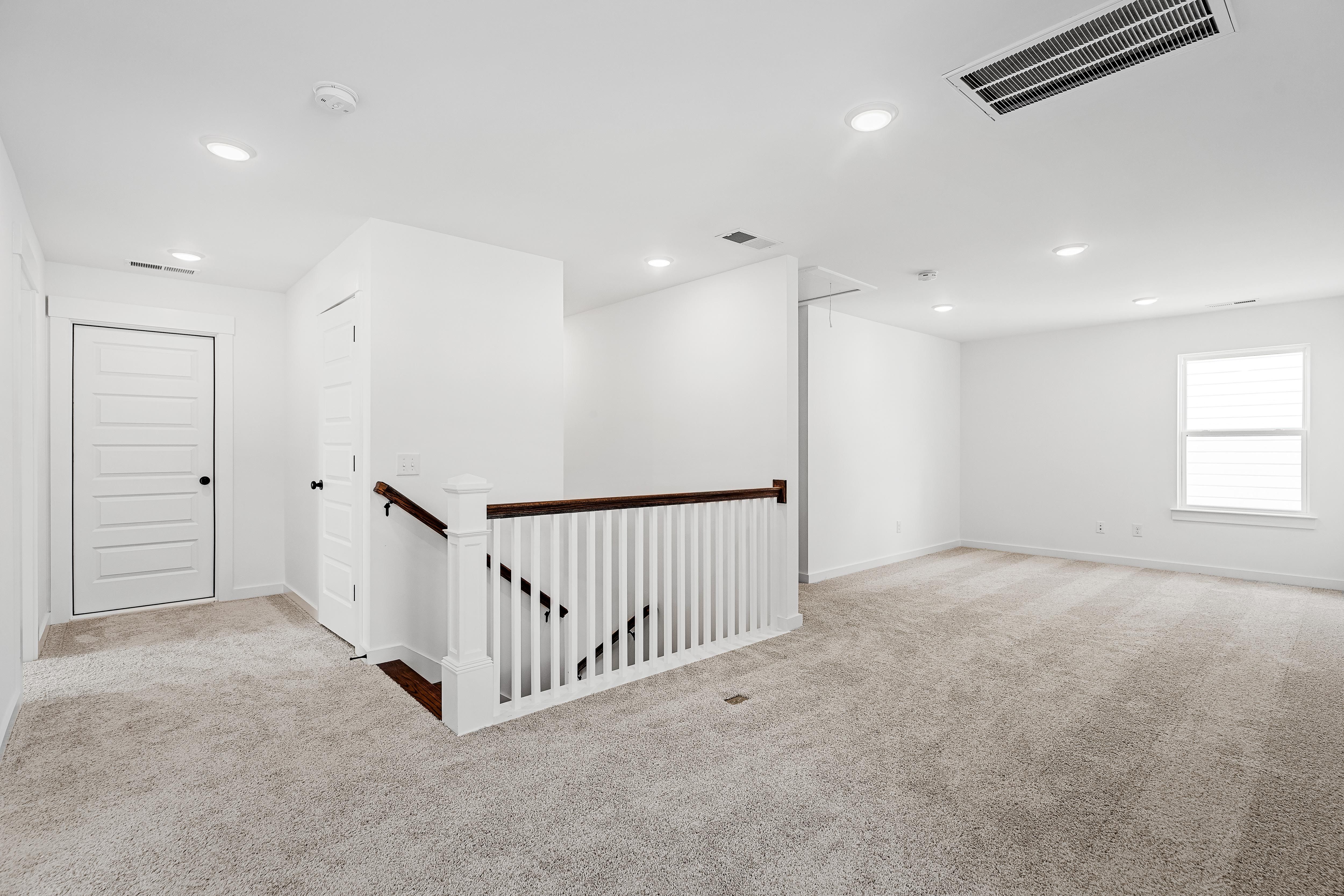 Spacious carpeted loft area on the second floor of The Cedar D home design featuring a white staircase railing.