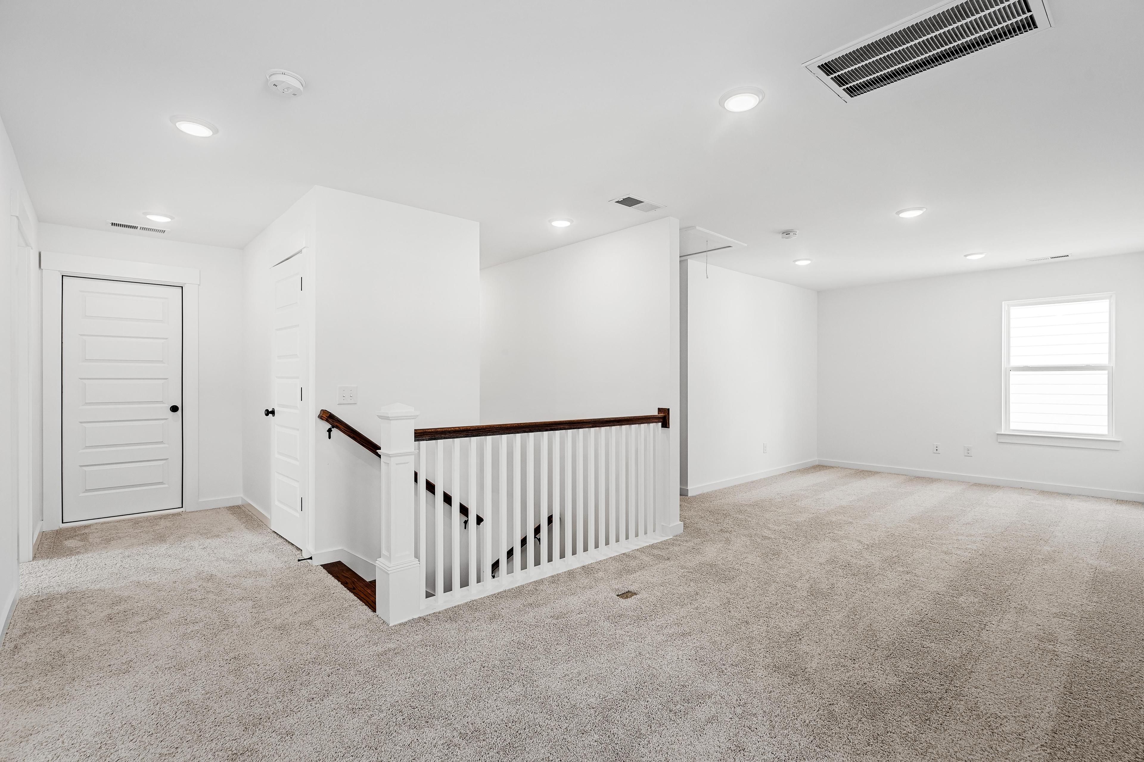 Spacious carpeted loft area on the second floor of The Cedar D home design featuring a white staircase railing.