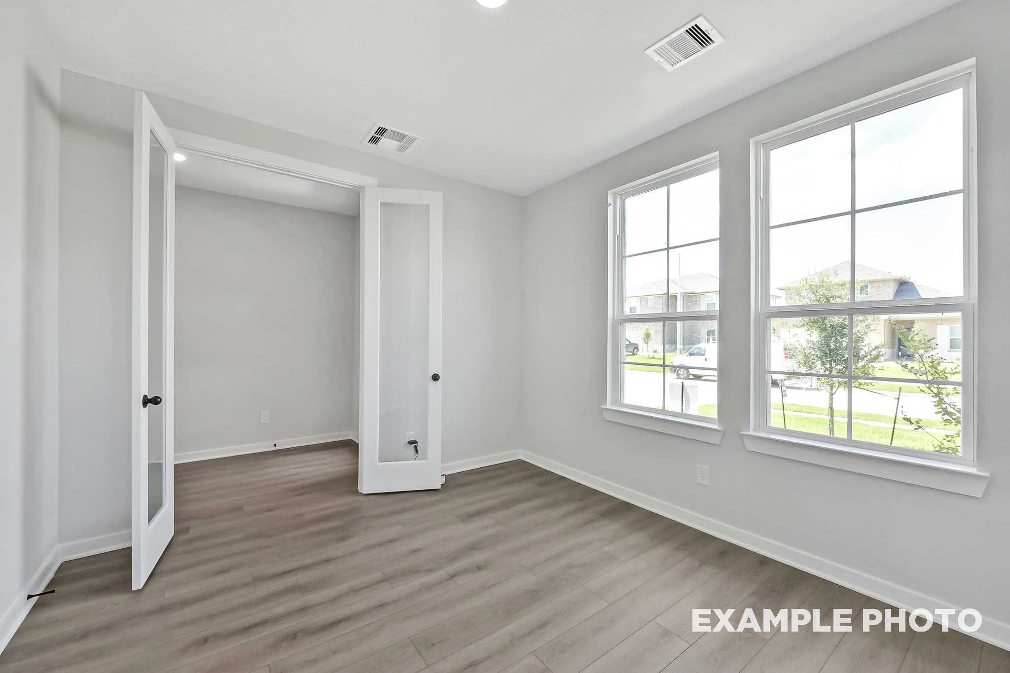 Bright Sequoia home interior showcasing open French doors, light gray walls, wood-look flooring, and large windows with yard view