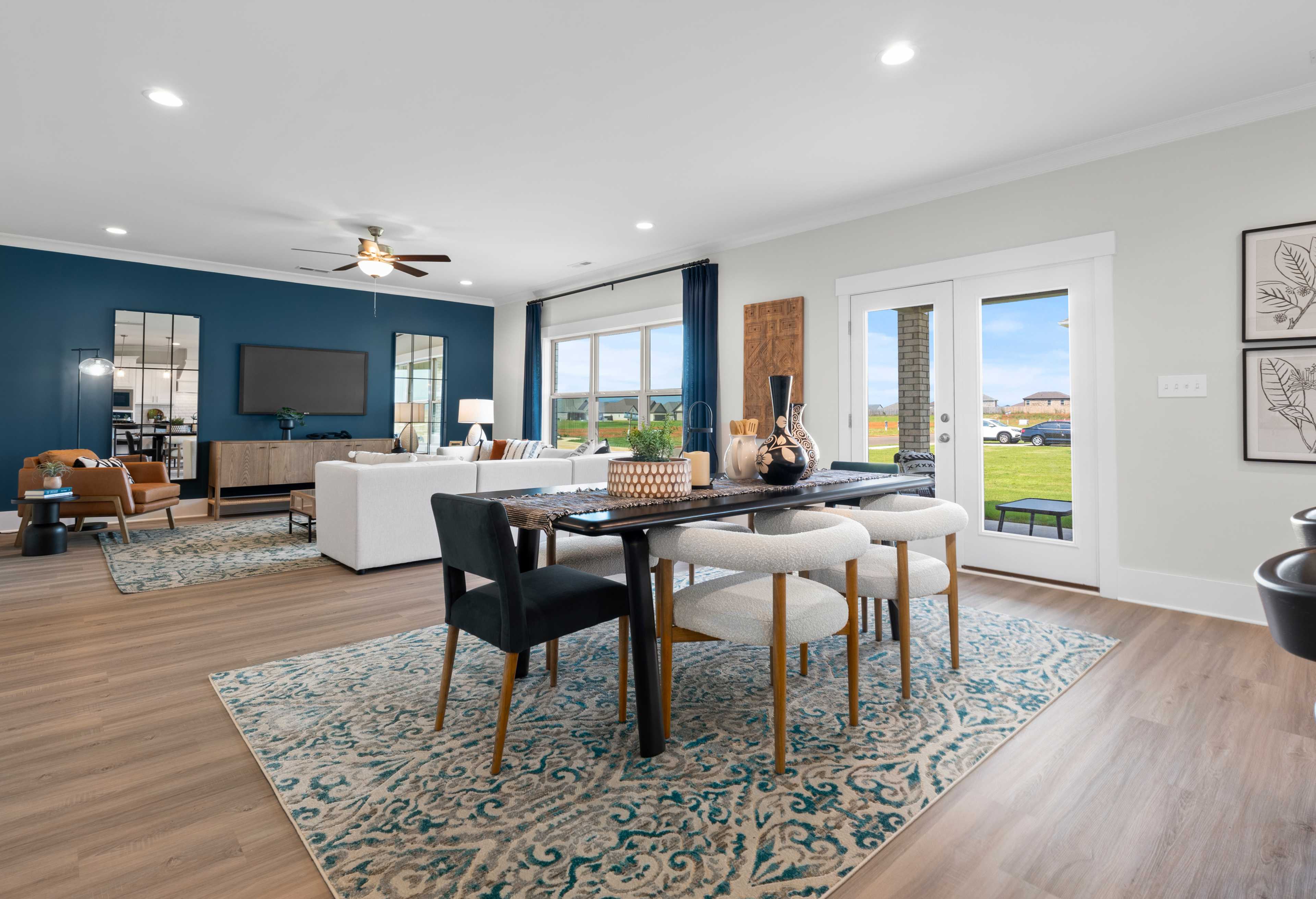 Spacious open-concept living dining in The Chelsea D with navy accent wall TV modern sofa wooden table chairs large sliding doors to green view