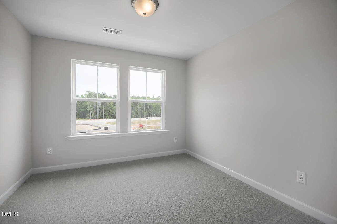 Bright, carpeted bedroom with neutral walls in The Mitchell Interior floor plan at Forestville Yard in Knightdale, NC.