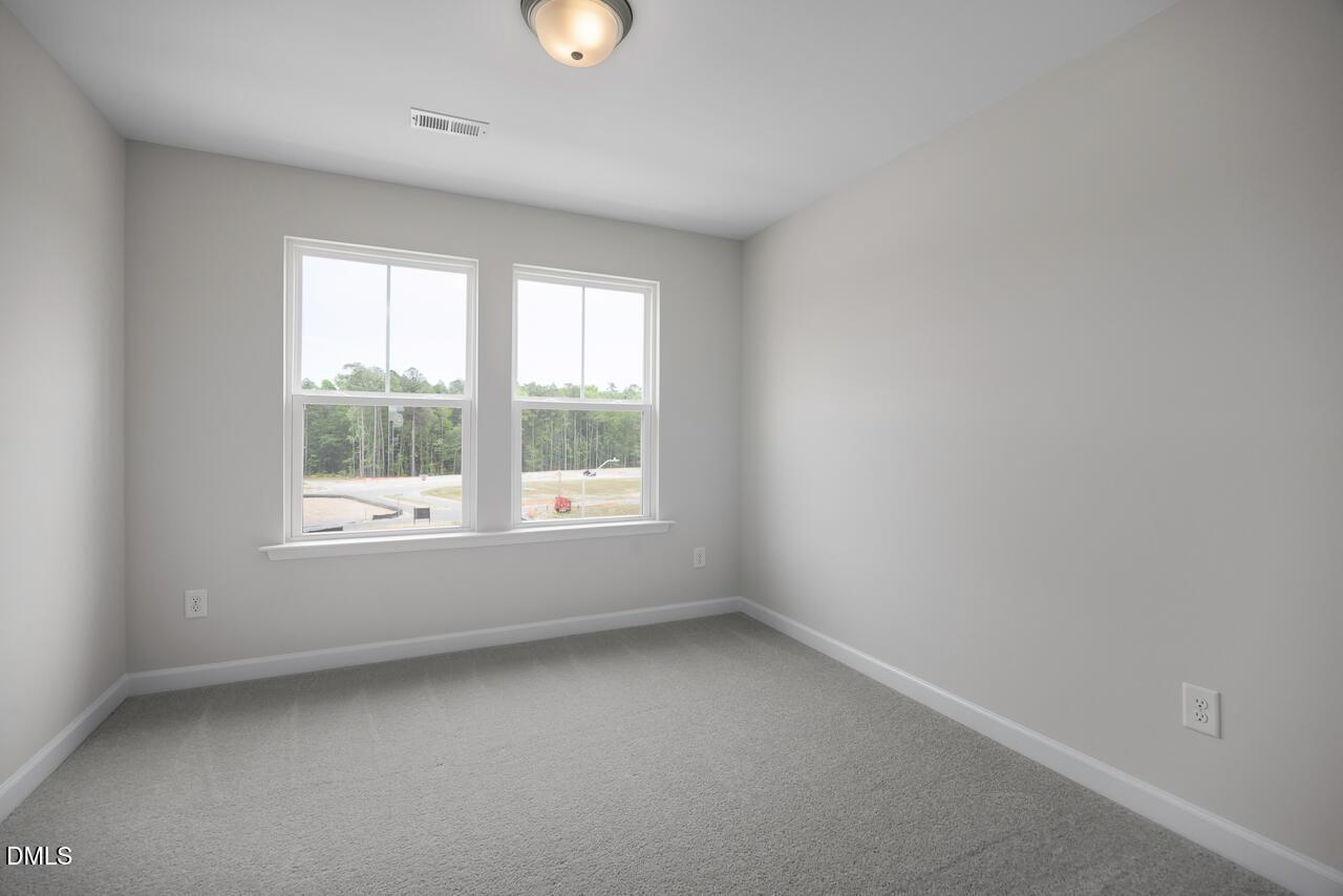 Bright, carpeted bedroom with neutral walls in The Mitchell Interior floor plan at Forestville Yard in Knightdale, NC.