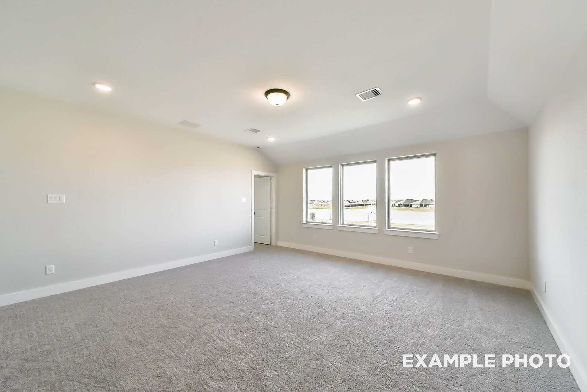 Bright secondary bedroom with vaulted ceiling, three large windows, beige walls, and gray carpet in Davidson Homes The Philip C, Rosharon, Texas