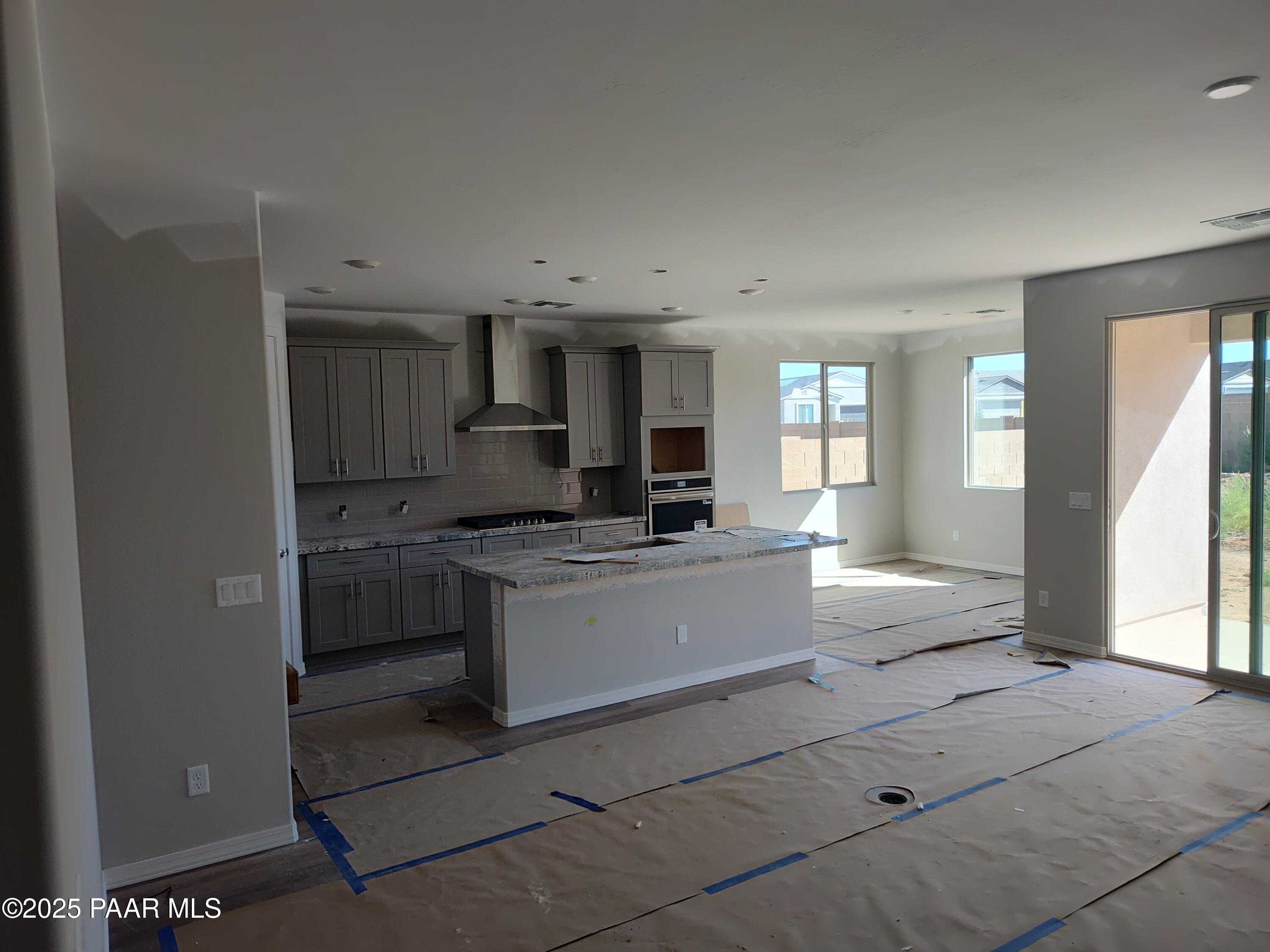 Spacious unfinished kitchen with gray cabinets, large white island, stainless range hood, and sliding doors to backyard in Davidson Homes The Harmony A, Prescott Valley, AZ