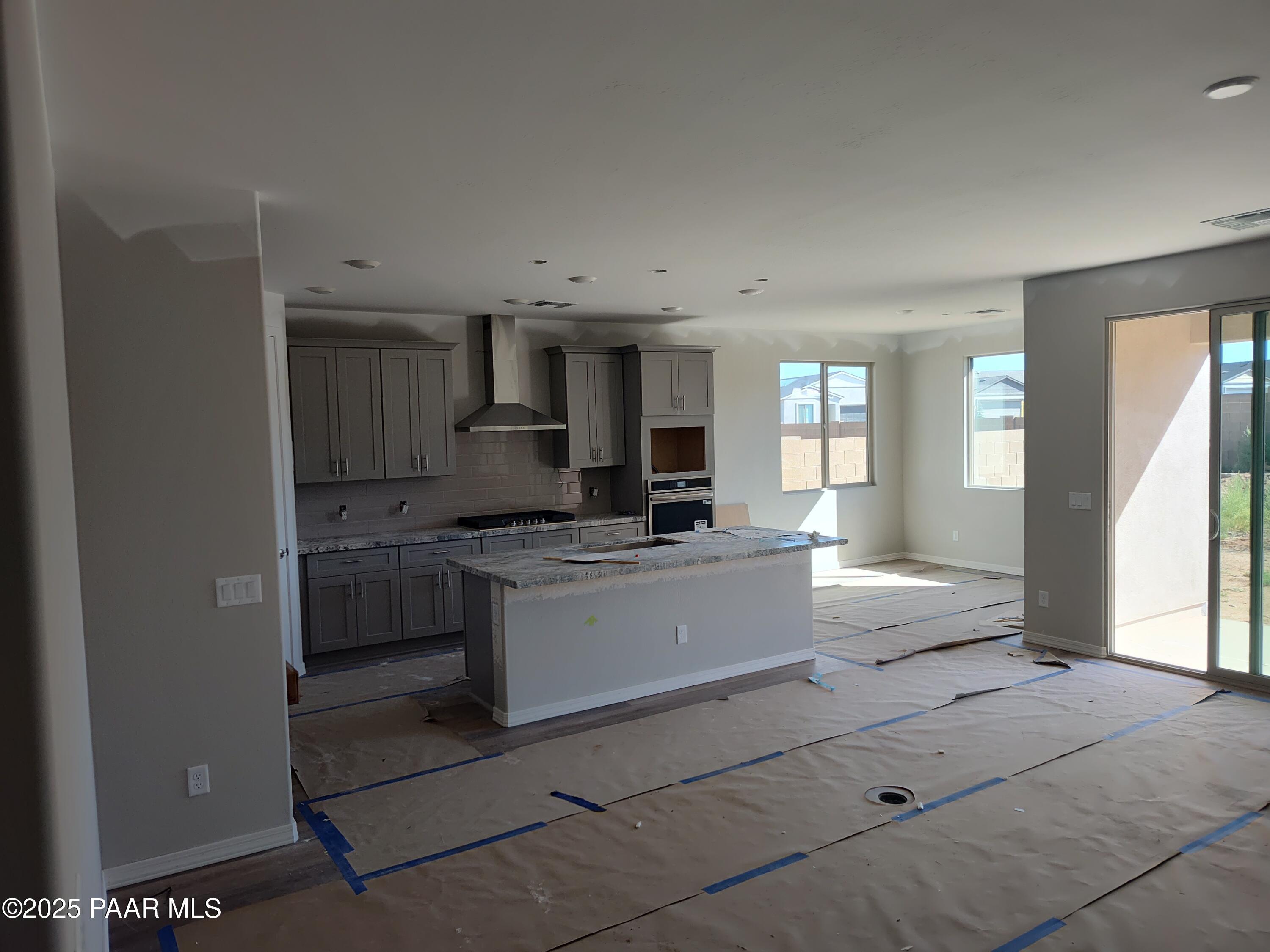 Spacious unfinished kitchen with gray cabinets, large white island, stainless range hood, and sliding doors to backyard in Davidson Homes The Harmony A, Prescott Valley, AZ