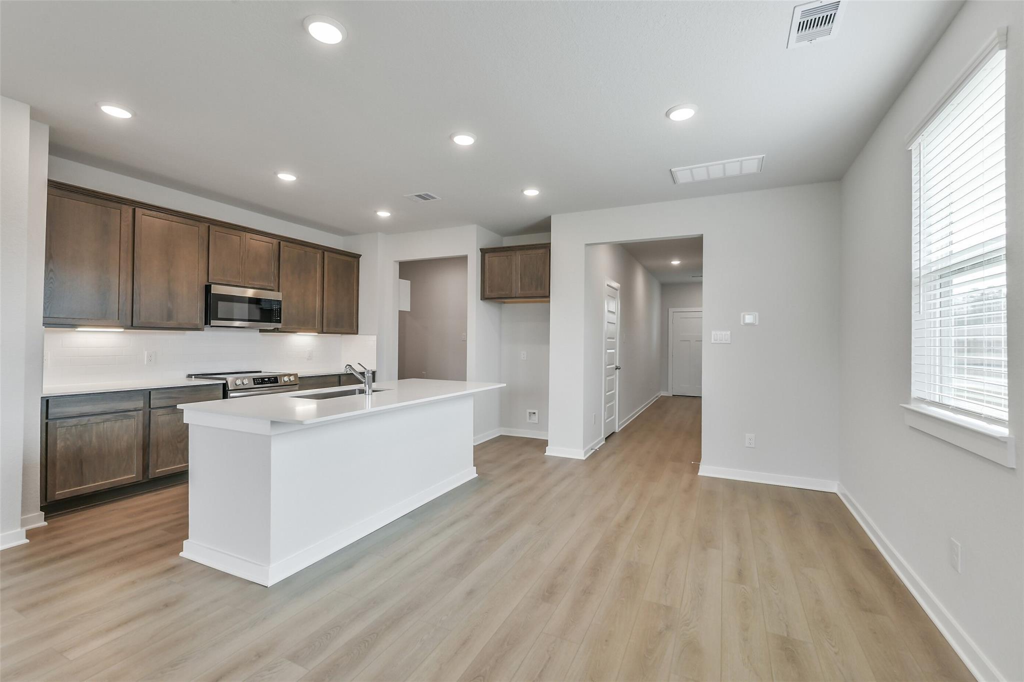 Modern kitchen featuring brown shaker cabinets, white quartz island, stainless appliances in The Brazos E 5-bedroom home, Cleveland, Texas