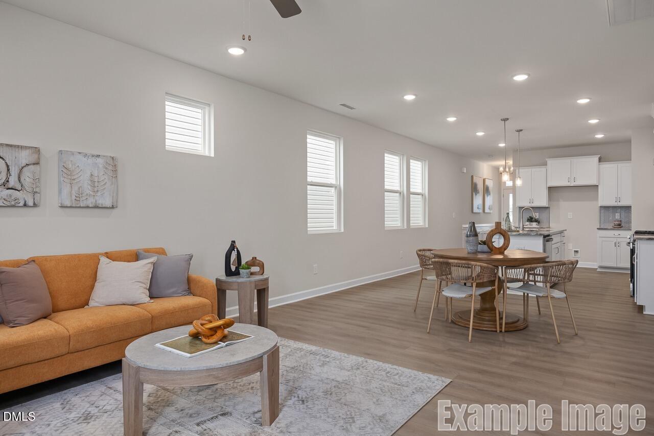Bright open-concept living room with orange sofa, round wooden dining table, and white kitchen cabinets in Davidson Homes Carter C, Lillington, NC