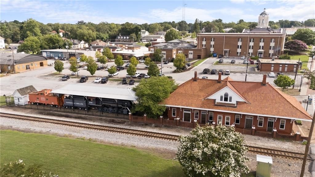 Aerial view of historic Winder Georgia train depot with red tile roof, railroad tracks, brick buildings, and downtown park near Lake Shore homes