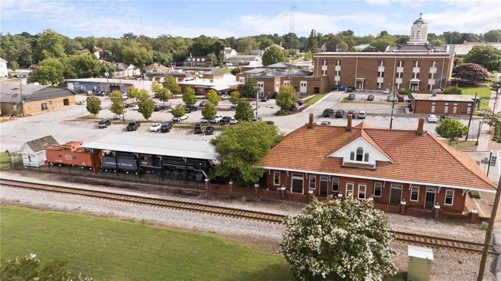 Aerial view of historic Winder Georgia train depot with red tile roof, railroad tracks, brick buildings, and downtown park near Lake Shore homes
