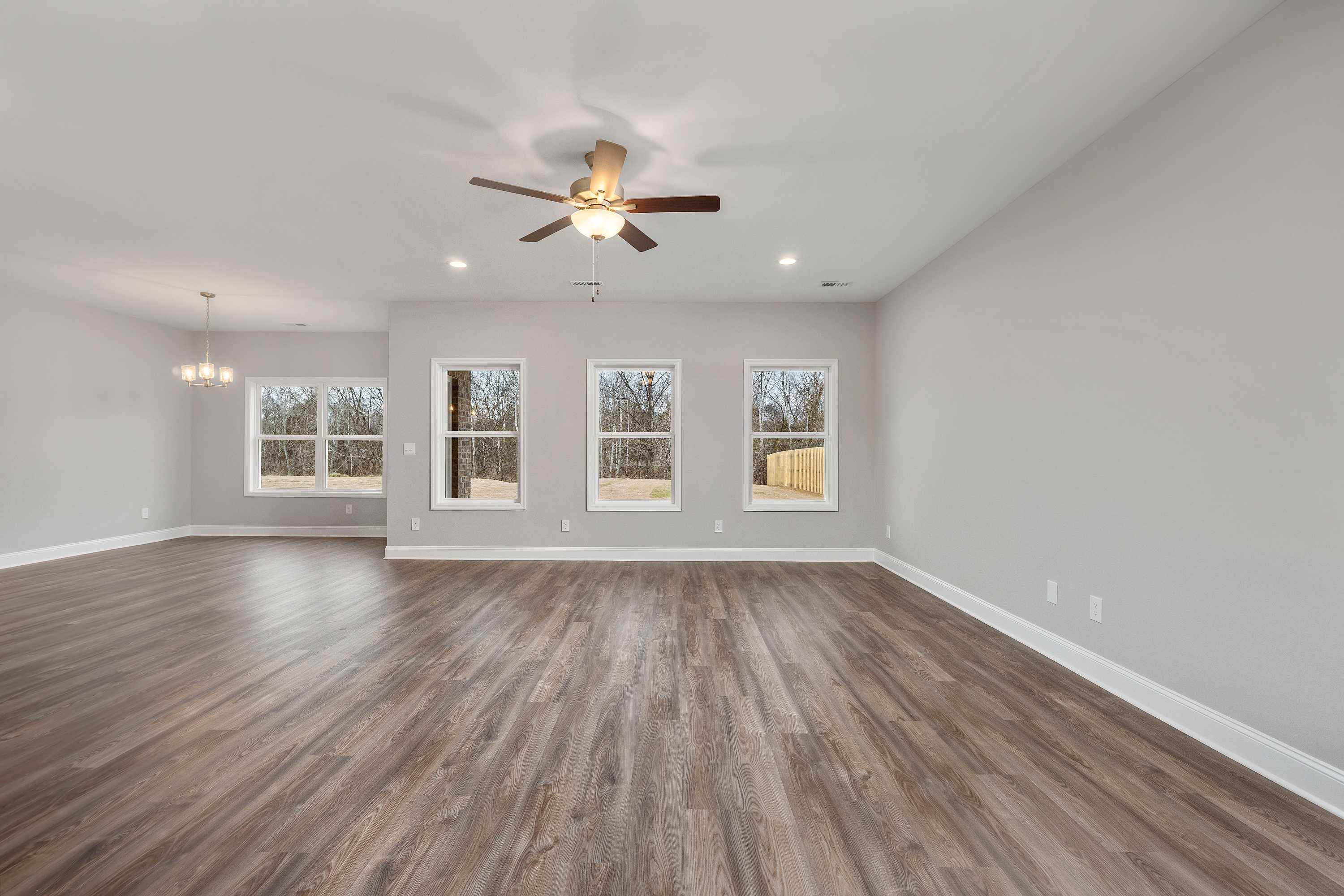 Spacious open-concept great room in The Aiken by Davidson Homes featuring light gray walls, hardwood floors, and large windows