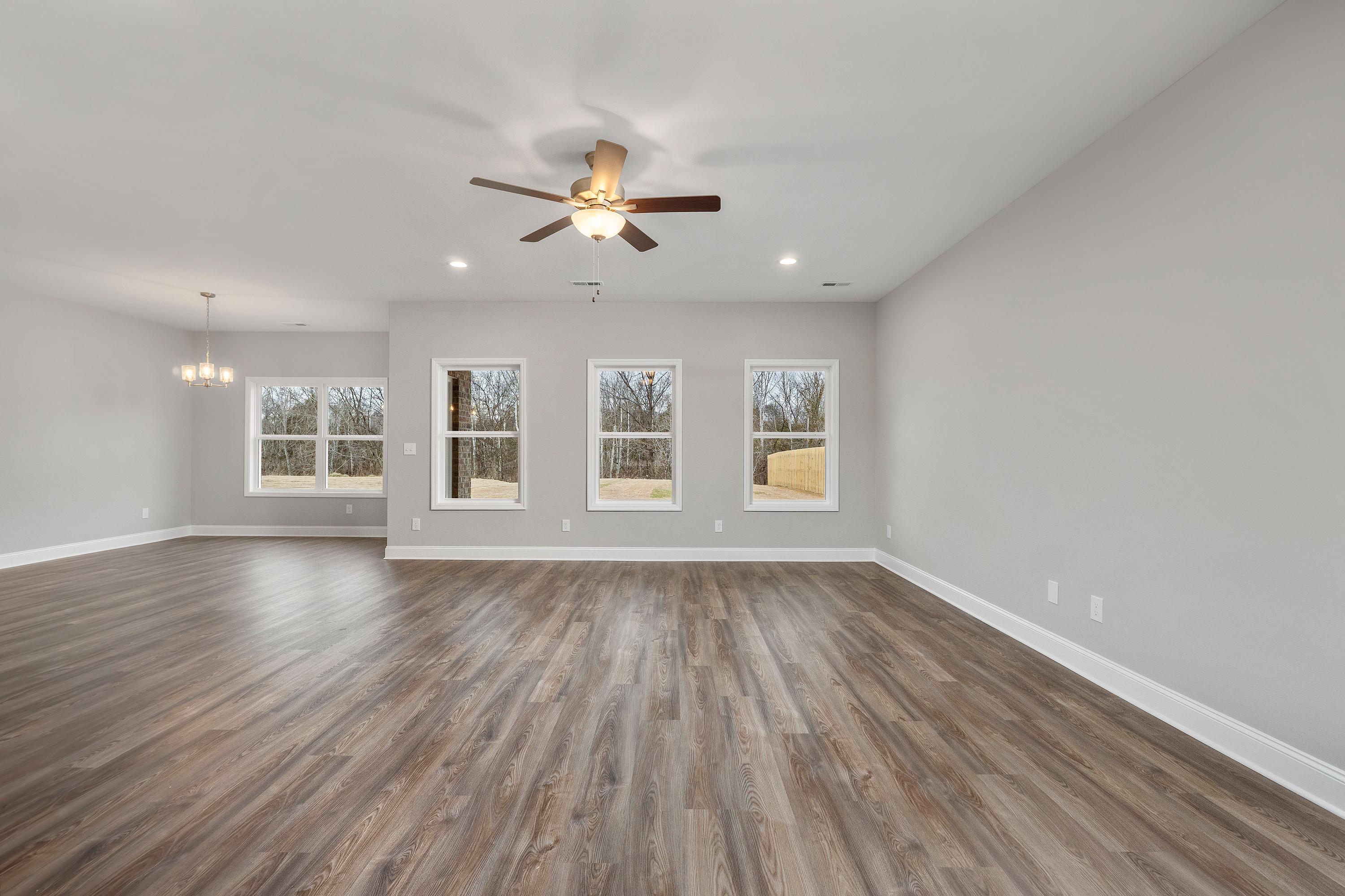 Spacious open-concept great room in The Aiken by Davidson Homes featuring light gray walls, hardwood floors, and large windows