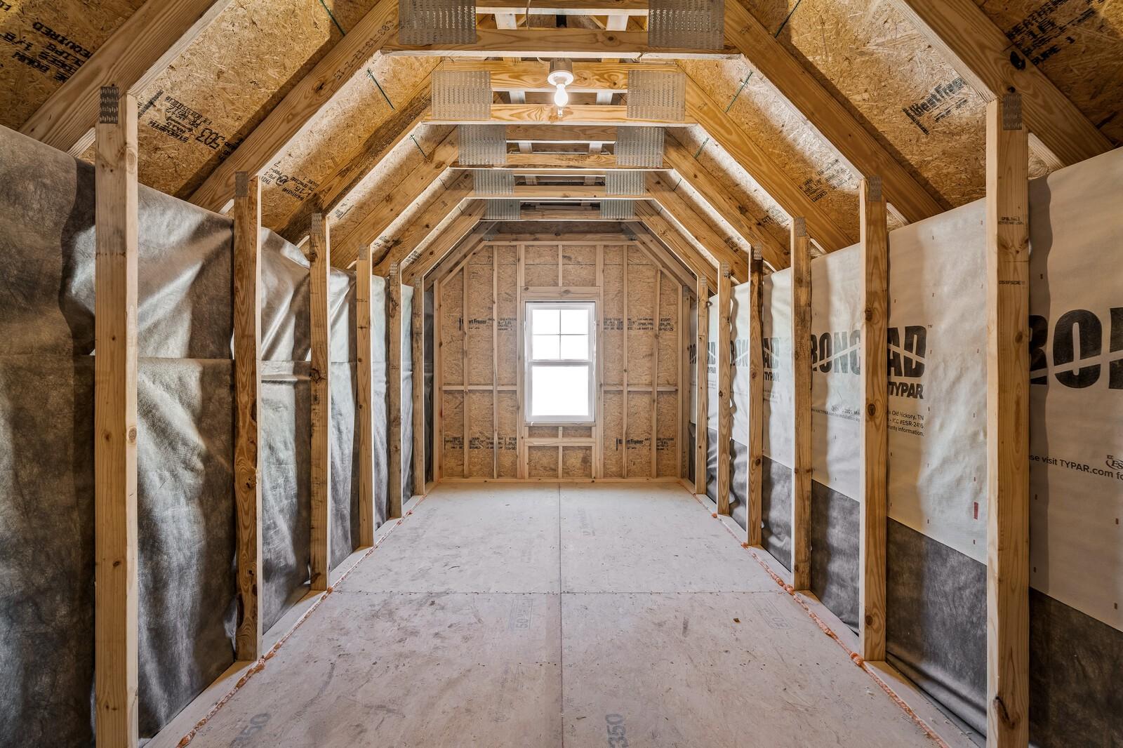 Unfinished bonus room with exposed wooden rafters, OSB panels, and window in Davidson Homes The Ash A, Gallatin, TN