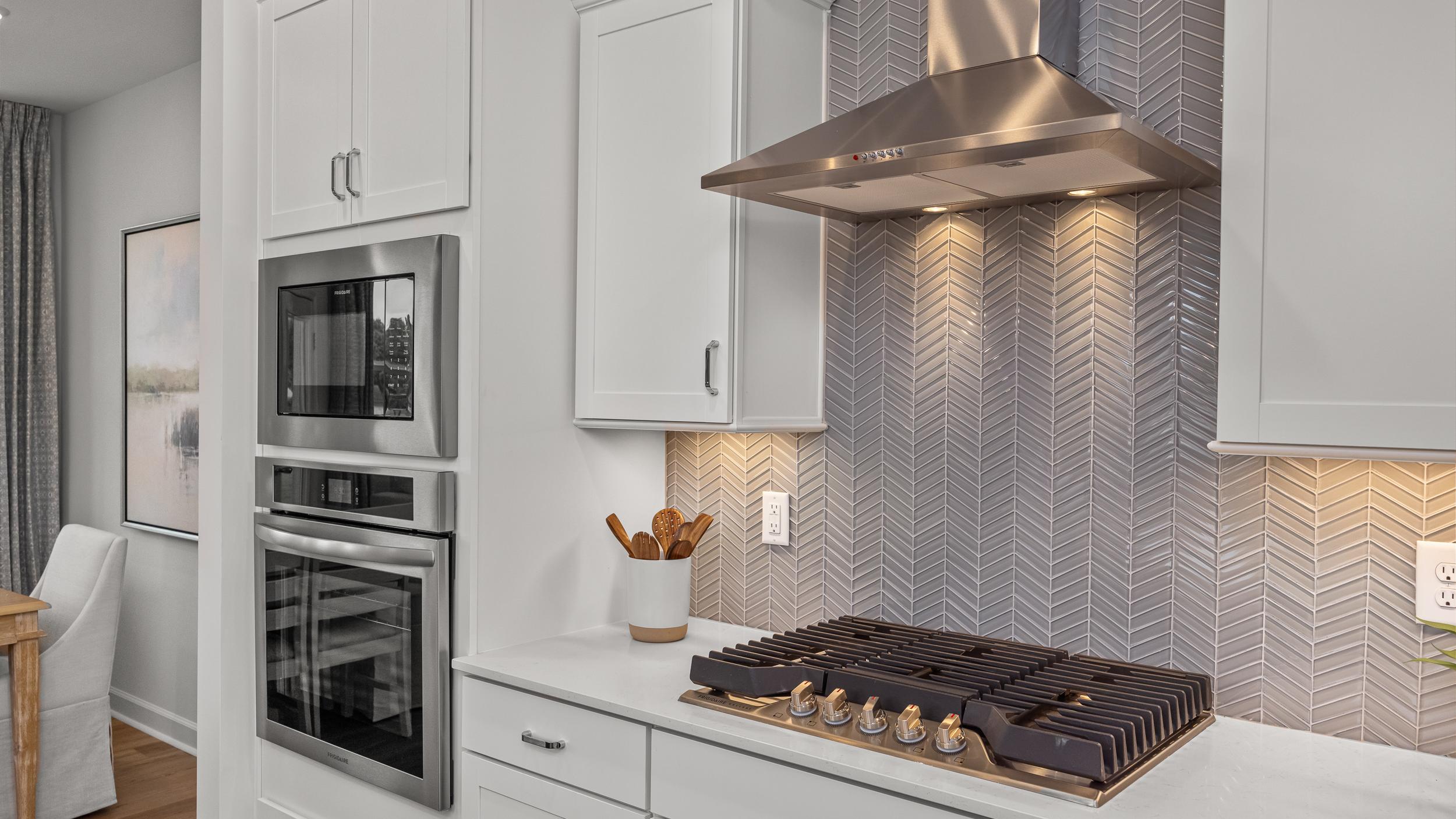 Modern kitchen at Forestville Yard Townhomes in Knightdale NC featuring white cabinets, stainless steel gas range, and herringbone tile backsplash