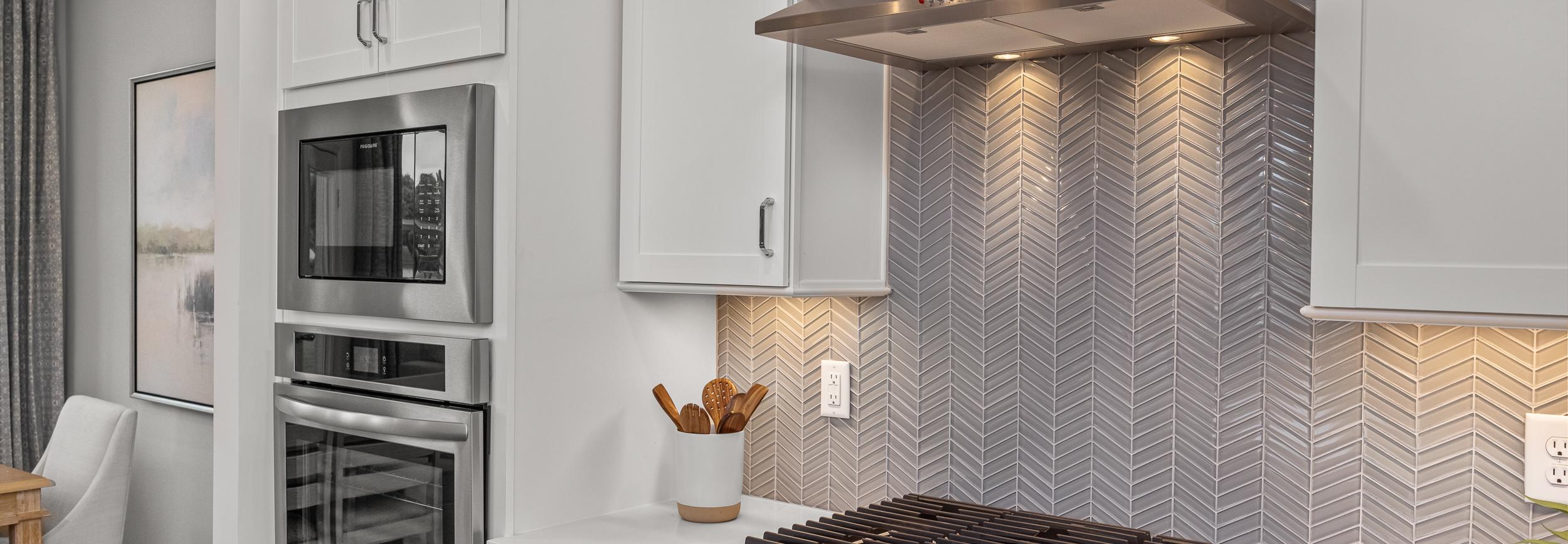 Modern kitchen at Forestville Yard Townhomes in Knightdale NC featuring white cabinets, stainless steel gas range, and herringbone tile backsplash