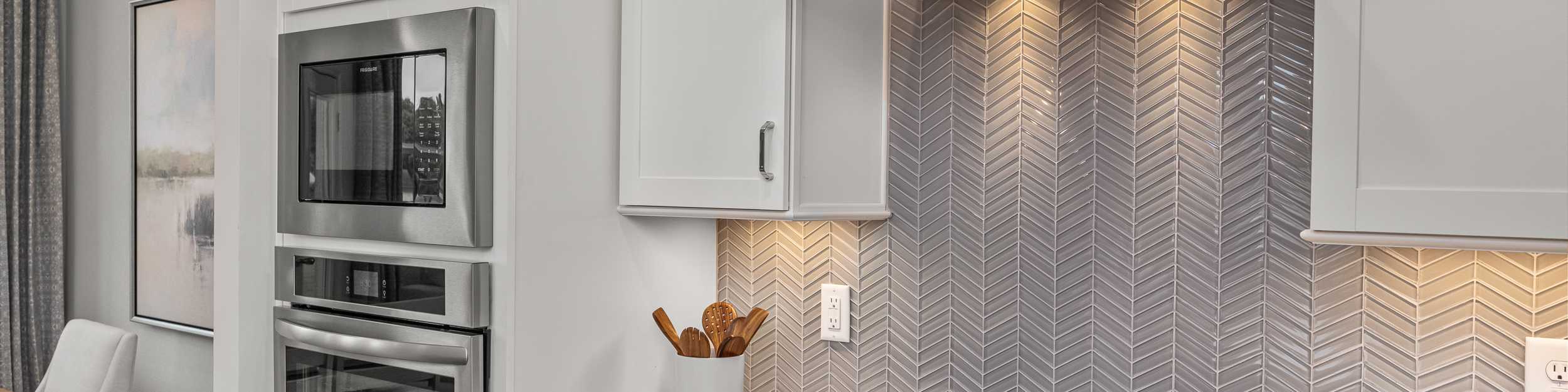Modern kitchen at Forestville Yard Townhomes in Knightdale NC featuring white cabinets, stainless steel gas range, and herringbone tile backsplash