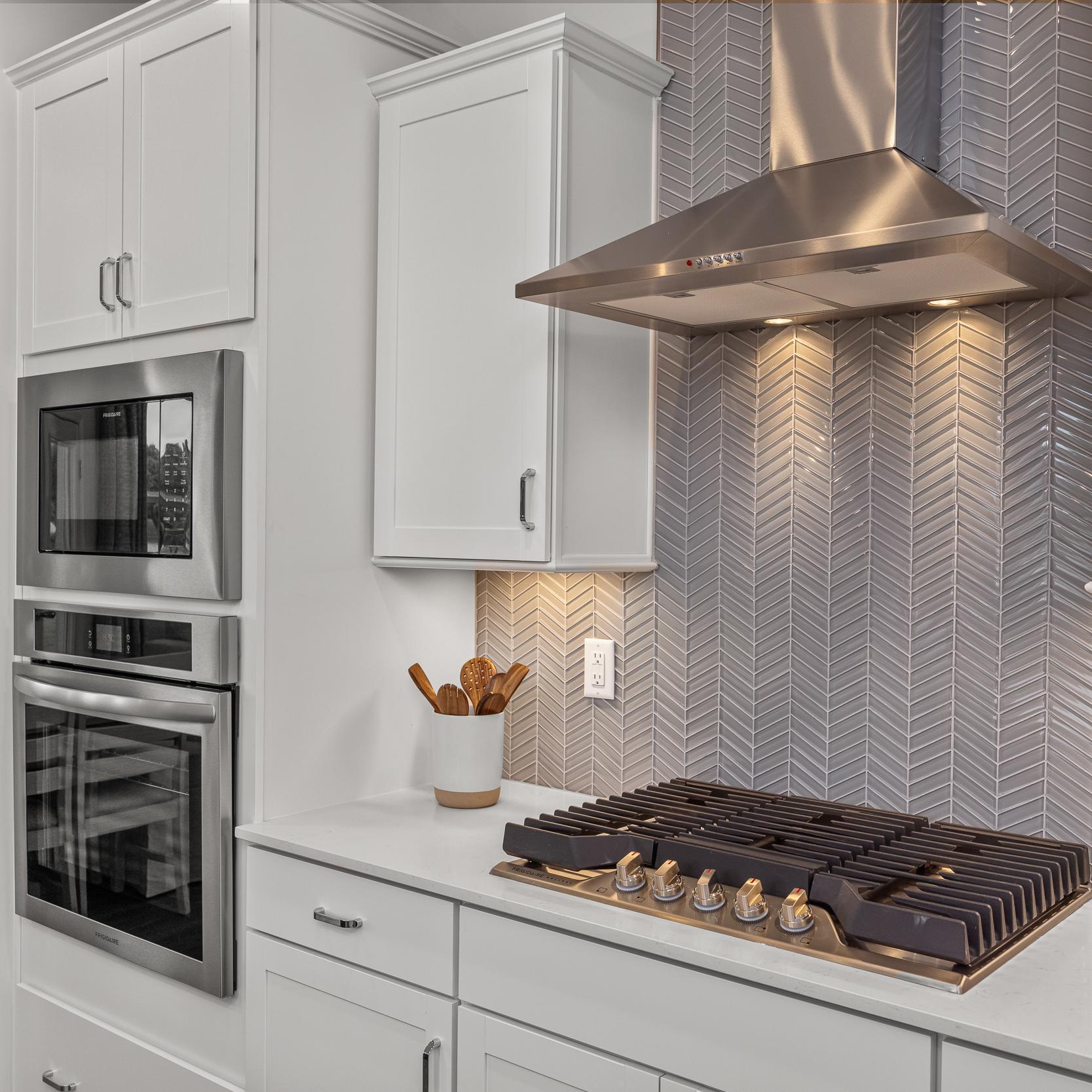 Modern kitchen at Forestville Yard Townhomes in Knightdale NC featuring white cabinets, stainless steel gas range, and herringbone tile backsplash