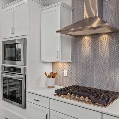 Modern kitchen at Forestville Yard Townhomes in Knightdale NC featuring white cabinets, stainless steel gas range, and herringbone tile backsplash
