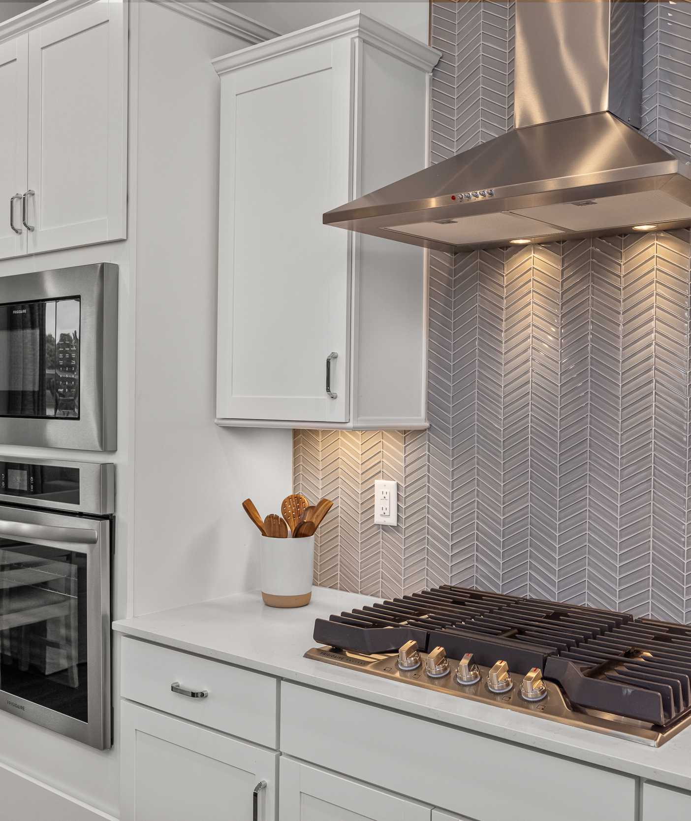Modern kitchen at Forestville Yard Townhomes in Knightdale NC featuring white cabinets, stainless steel gas range, and herringbone tile backsplash