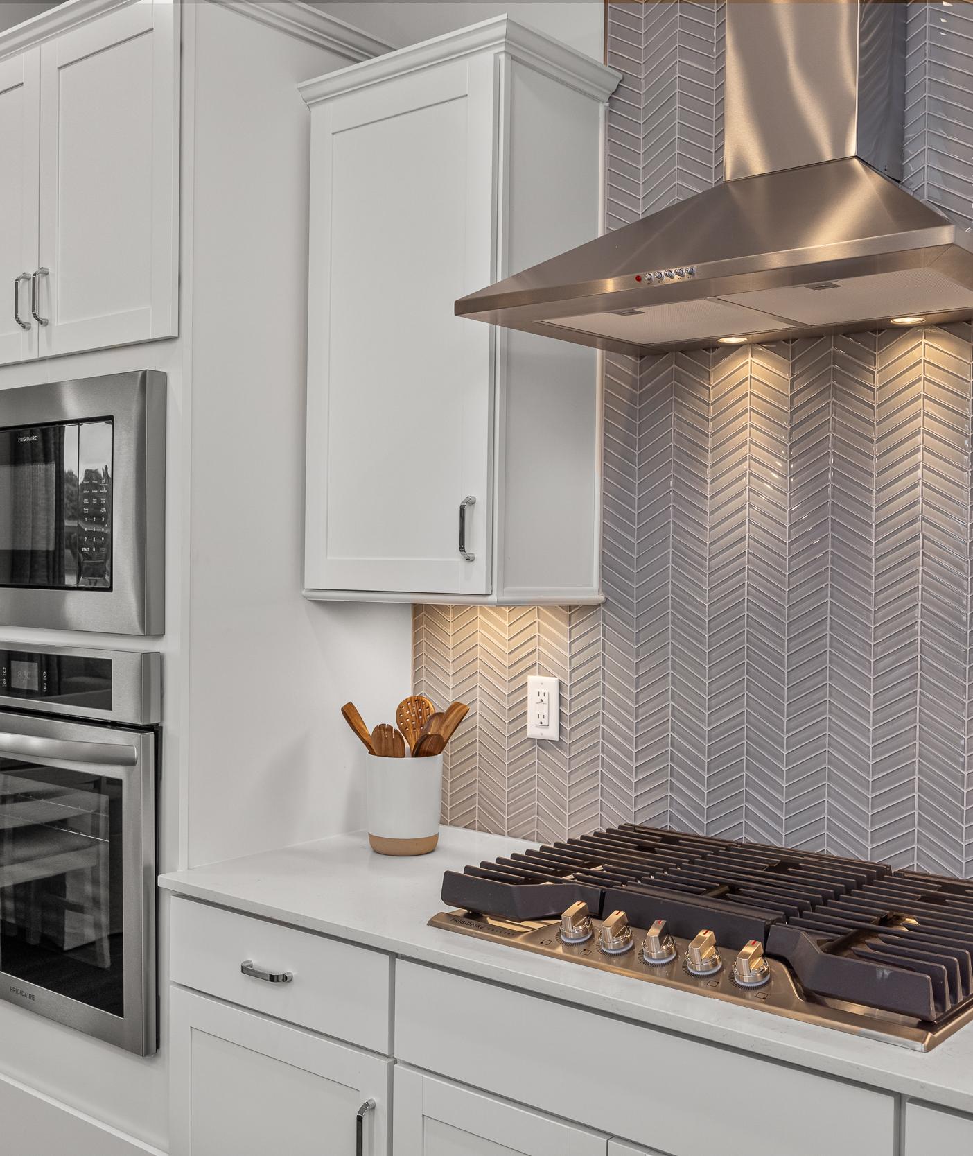 Modern kitchen at Forestville Yard Townhomes in Knightdale NC featuring white cabinets, stainless steel gas range, and herringbone tile backsplash
