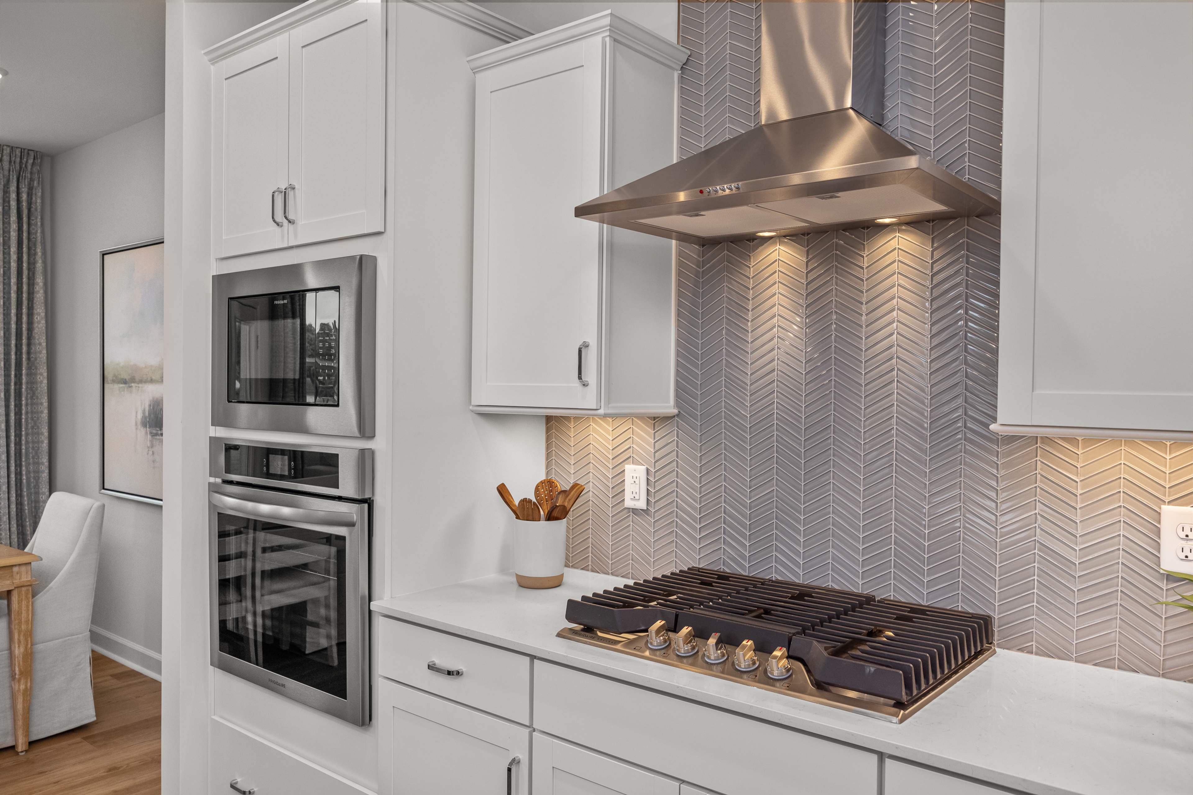 Modern kitchen in Bradford Raleigh NC with white shaker cabinets, stainless steel range, and gray herringbone backsplash