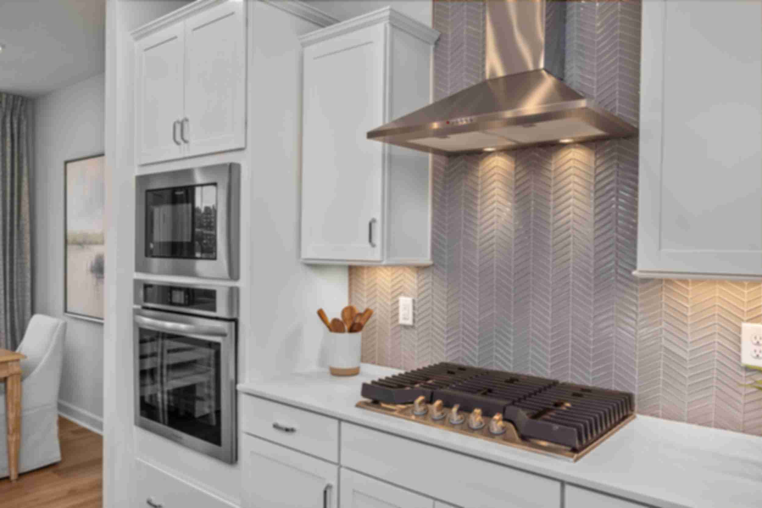 Modern kitchen at Forestville Yard Townhomes in Knightdale NC featuring white cabinets, stainless steel gas range, and herringbone tile backsplash