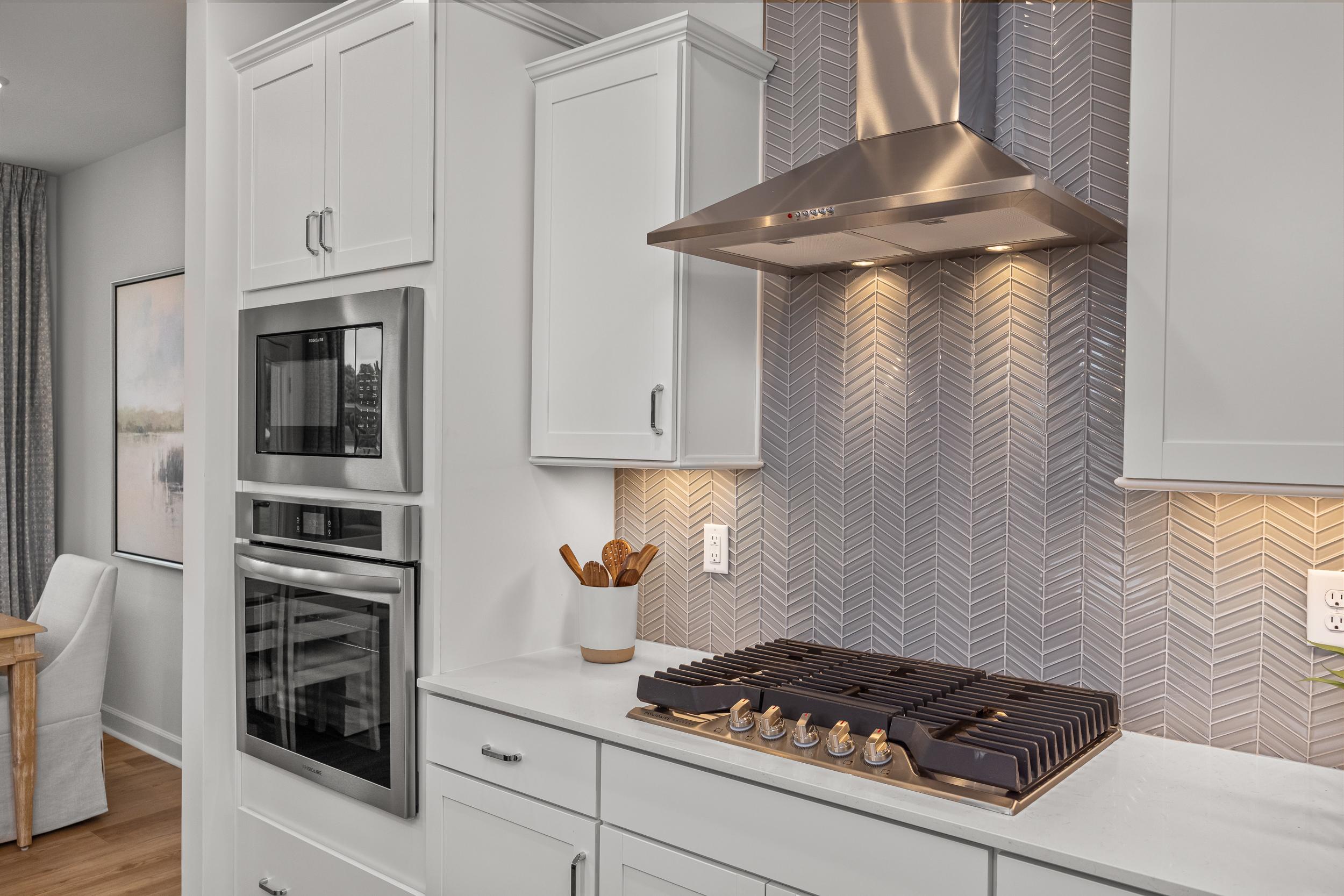 Modern Springvale kitchen in Fuquay-Varina NC featuring white cabinets, stainless steel gas range, oven, and gray herringbone backsplash
