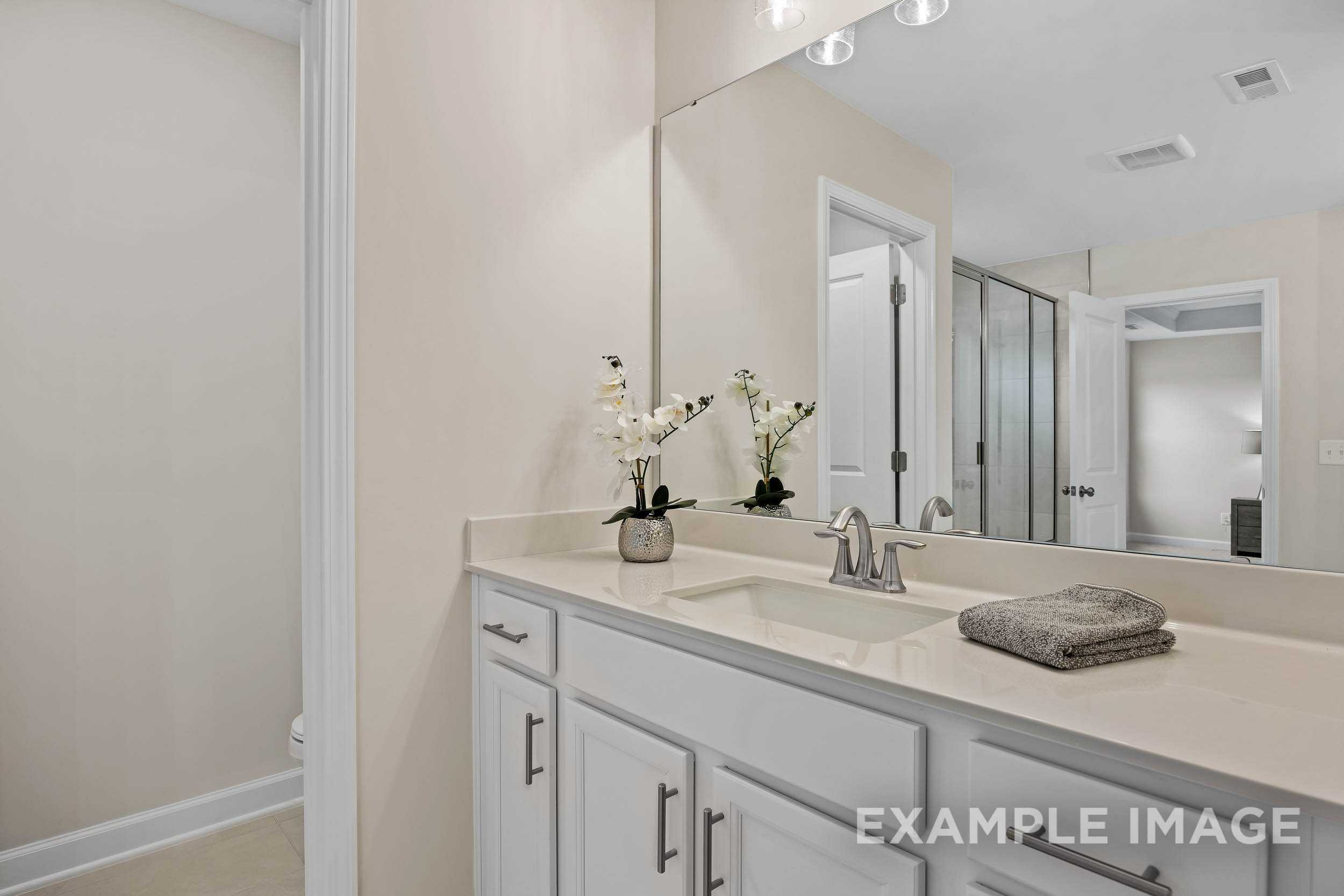 Spacious master bathroom in The Preston A with double vanity, large mirror, and glass shower enclosure